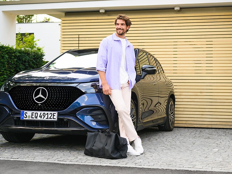 Een persoon leunt tegen een Mercedes-Benz voertuig voor zijn woning.