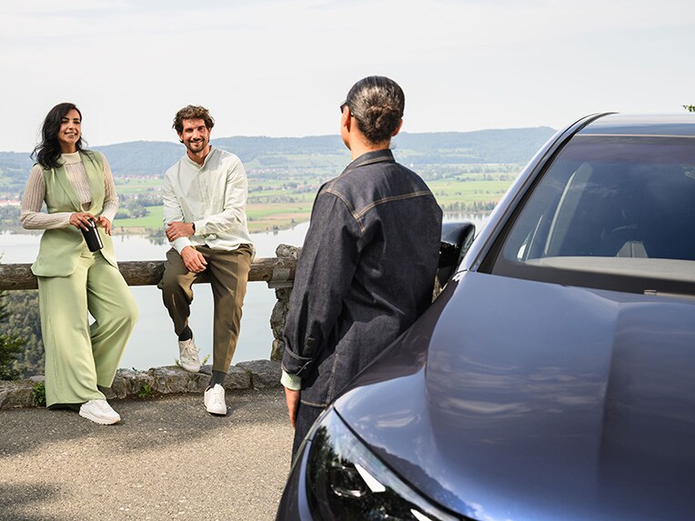 Une personne appuyée sur un véhicule Mercedes-Benz parlant à deux autres personnes appuyées sur une clôture.