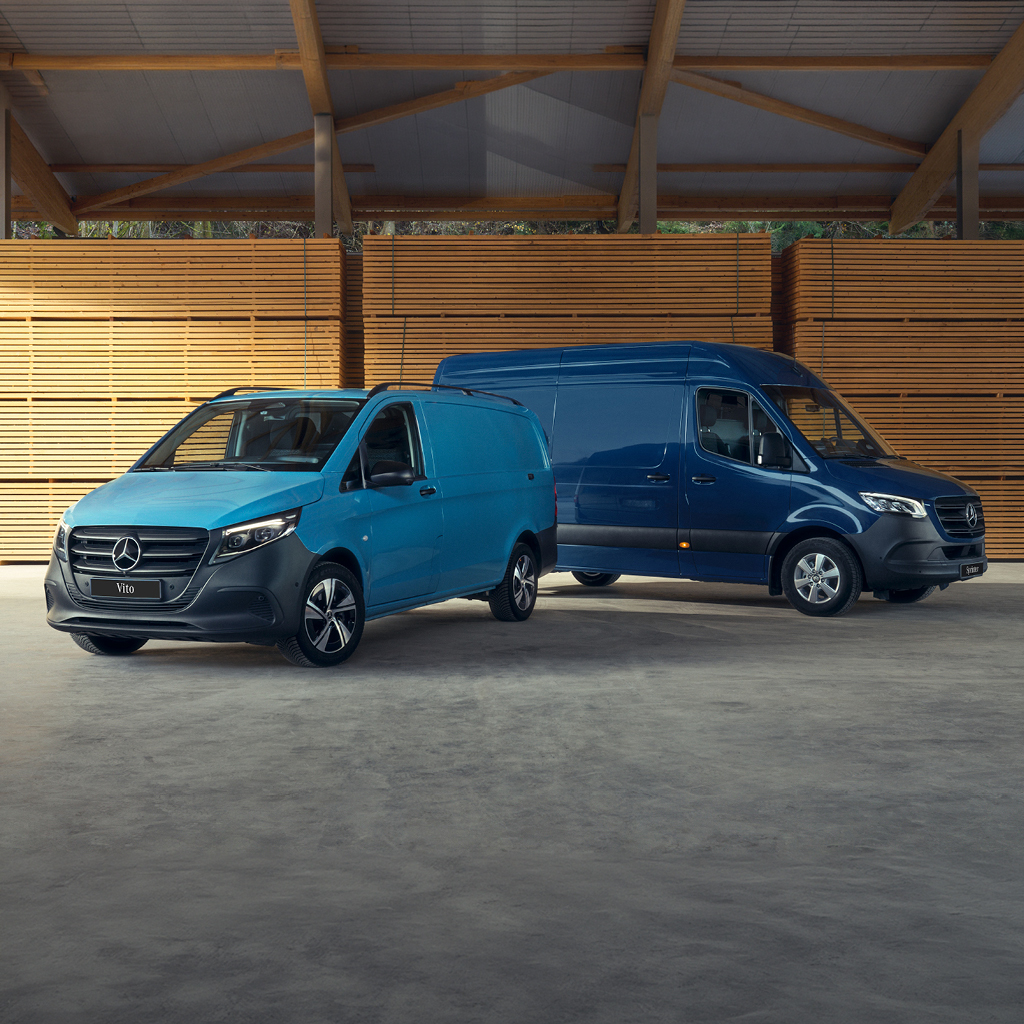 Twee blauwe Mercedes-Benz bestelwagens in een houten loods.