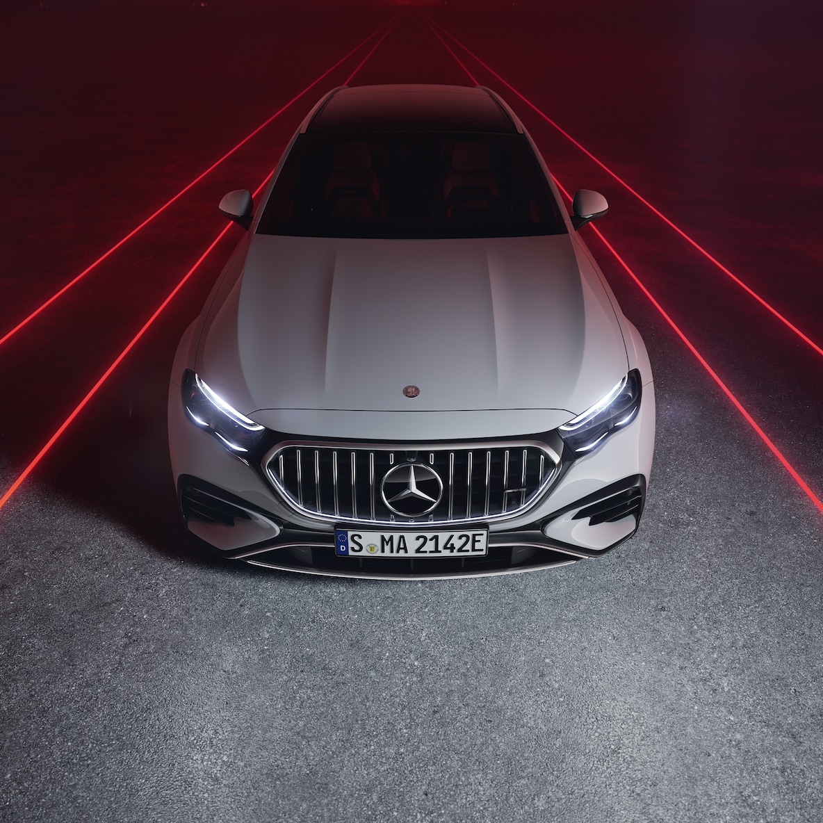 Vooraanzicht van de Mercedes-AMG E 53 HYBRID 4MATIC+ tegen een rode achtergrond, van bovenaf gezien.