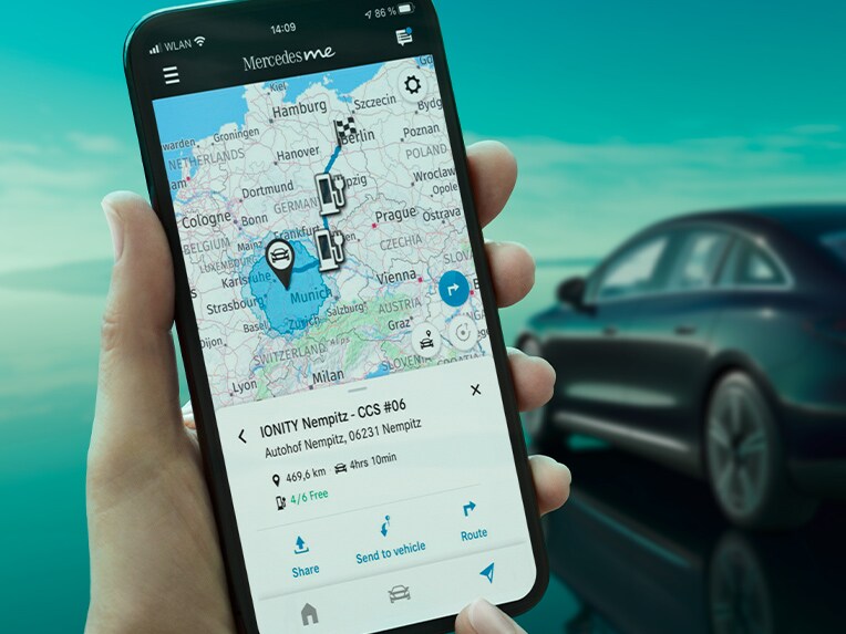 L'application ECO Coach sur un smartphone et, en arrière-plan, l'EQE Berline en charge sur un boîtier mural.