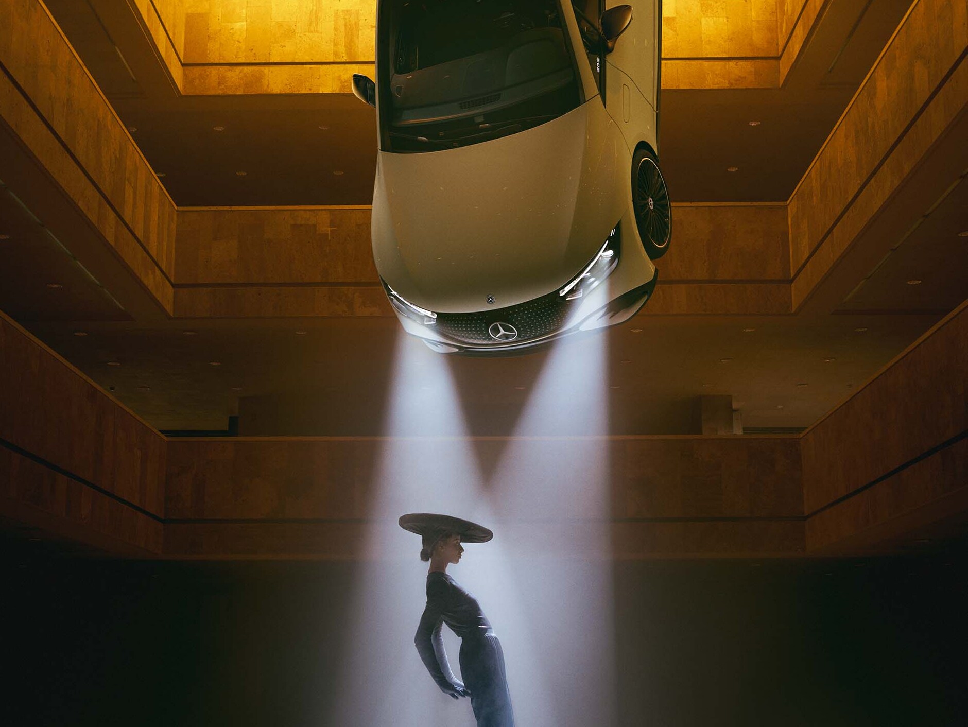 Une pièce sombre, au plafond de laquelle sont suspendus des projecteurs dans le faisceau desquels se tient une femme.