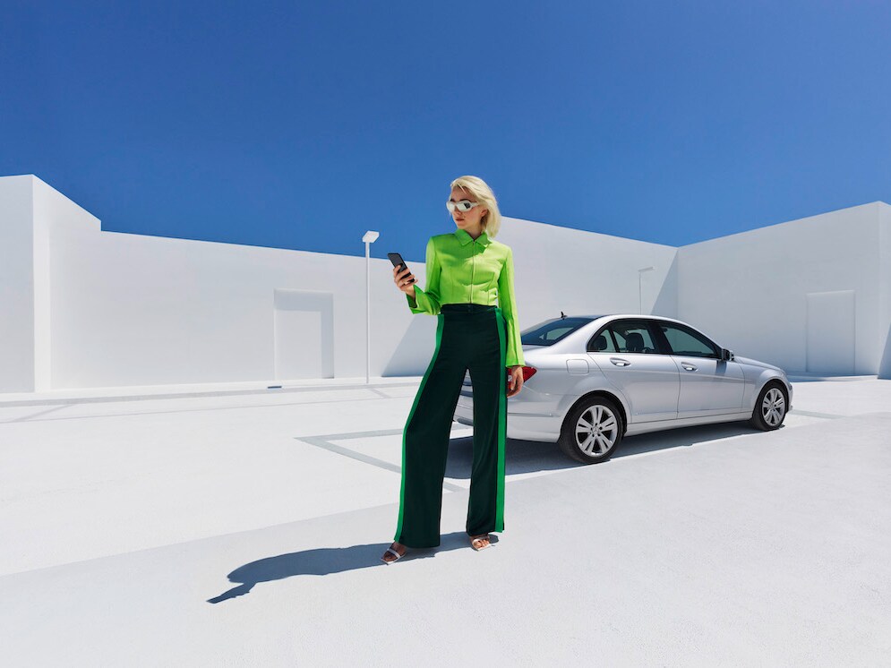 Une femme se tient devant sa Mercedes-Benz et consulte son smartphone.