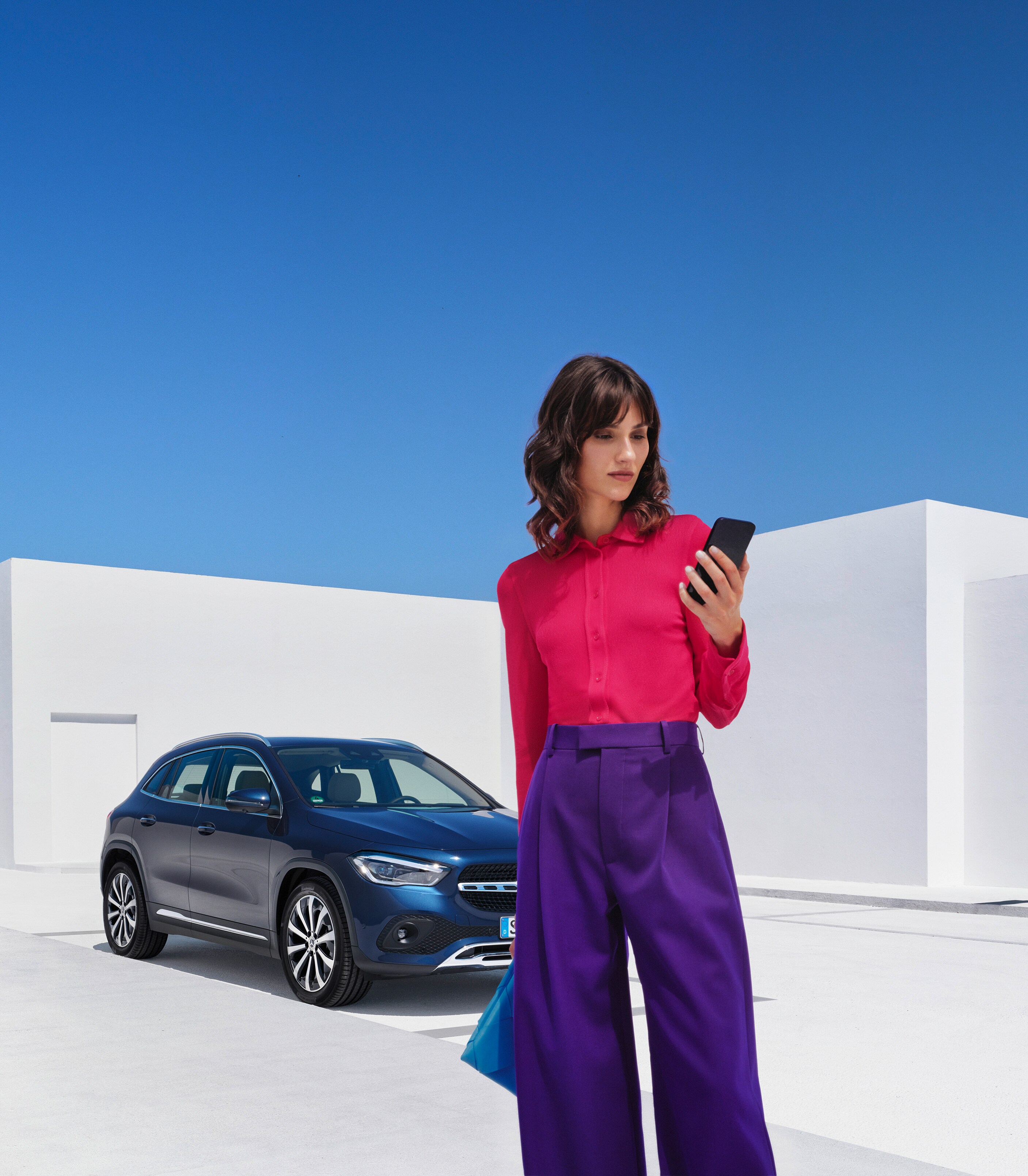 Une femme se tient devant sa Mercedes-Benz et consulte son smartphone.