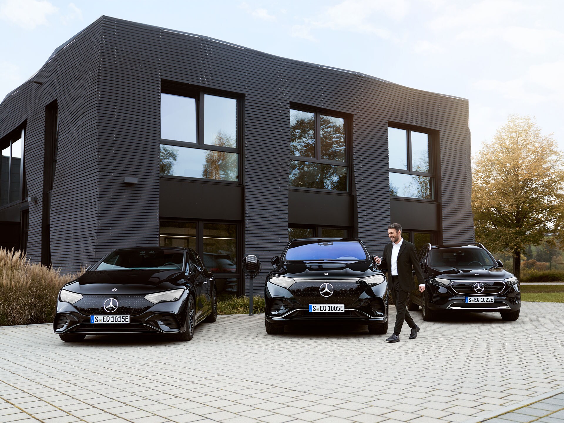 Trois véhicules électriques Mercedes-Benz devant un immeuble de bureaux.