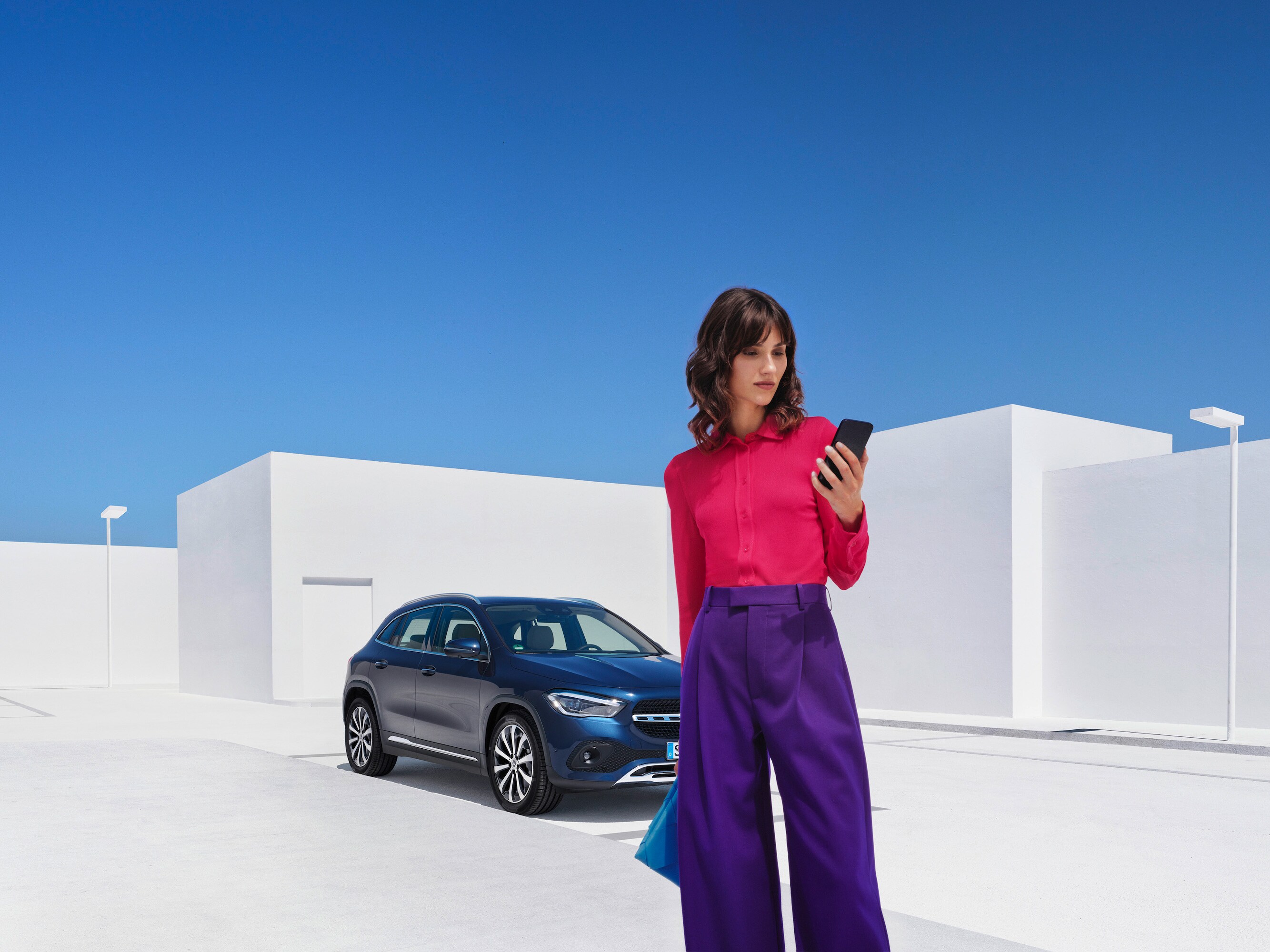 Een vrouw staat met haar smartphone vóór haar Mercedes-Benz.