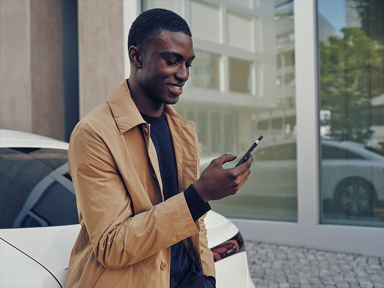 Un homme tenant son smartphone à la main, à côté d'une voiture électrique Mercedes-Benz.
