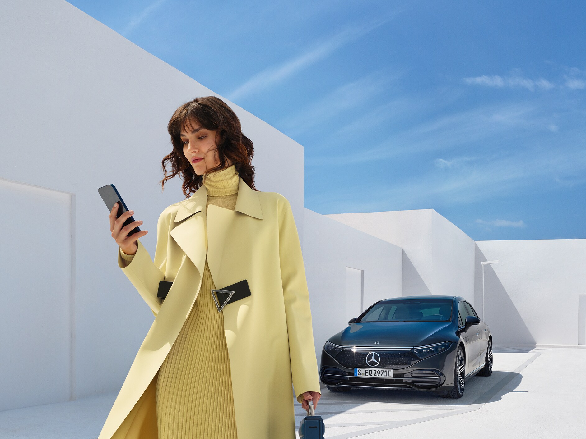 Vrouw kijkt naar haar mobiele telefoon terwijl ze wegloopt van haar Mercedes-Benz met EQ-technologie.