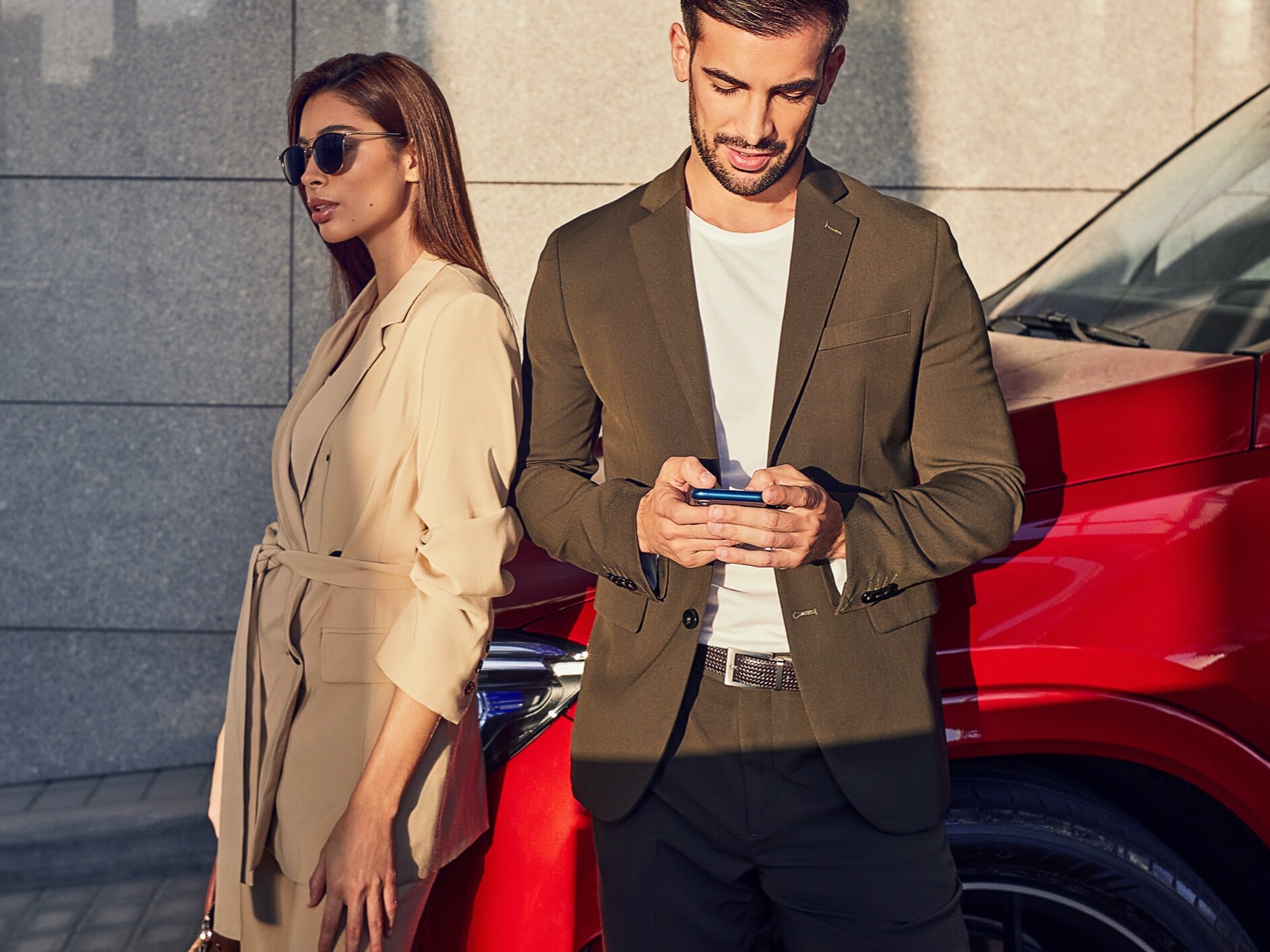 Une femme et un homme sont appuyés contre une Mercedes-Benz. L’homme est connecté au véhicule via son smartphone et des offres digitales.
