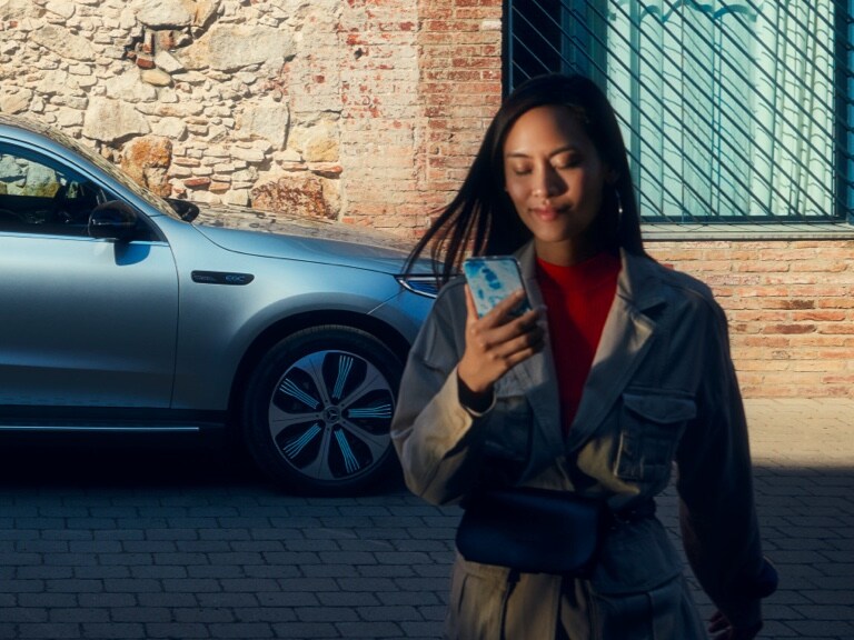 Une femme utilise l’application Mercedes me sur son smartphone pour se connecter à sa Mercedes-Benz.