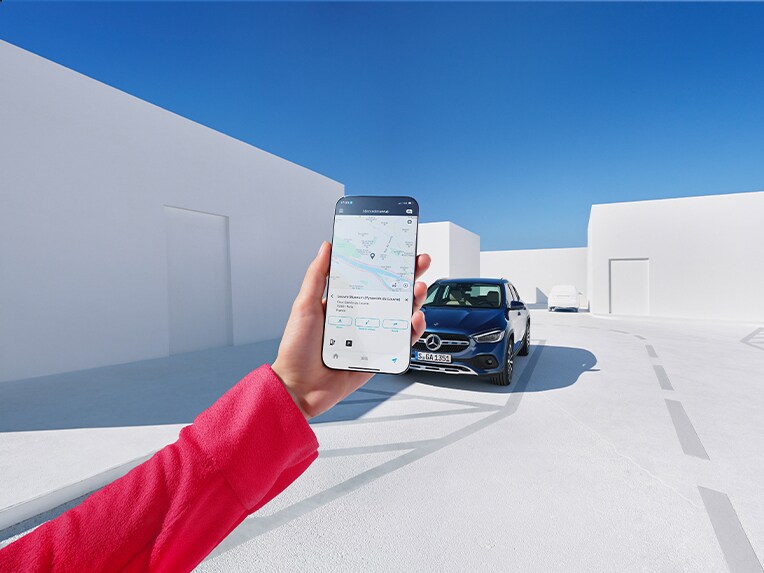 Een vrouw laat zich via de Mercedes me App op haar smartphone en de digitale extra's voor navigatie informeren wat de weersverwachting op de bestemming is.