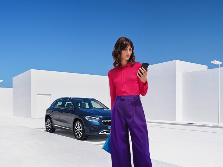 Een vrouw brengt via haar smartphone en de Mercedes me App een verbinding met haar Mercedes-Benz tot stand en controleert met de digitale extra's voor remote of alle portieren zijn vergrendeld.