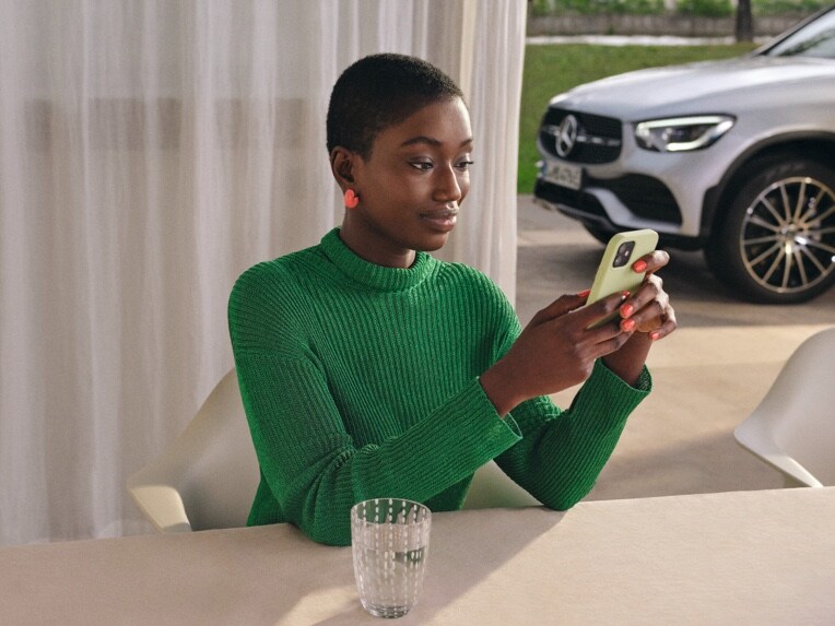 Une femme regarde son smartphone, qui est relié à sa Mercedes-Benz par des offres digitales.