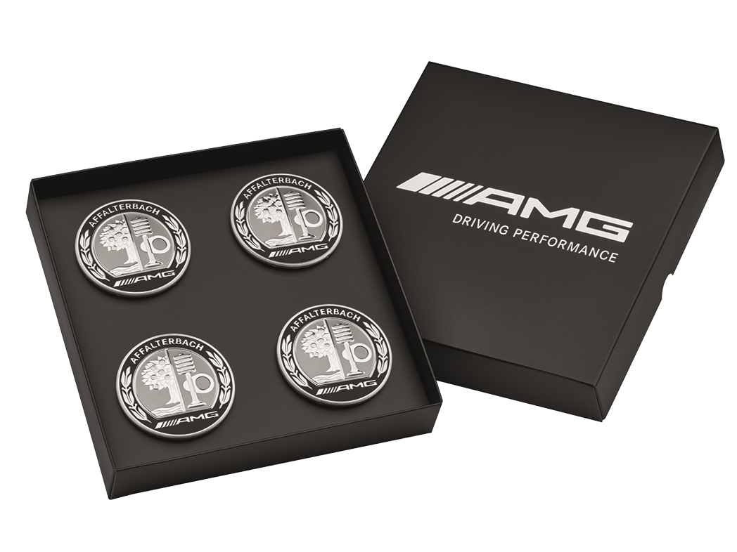 Quatre enjoliveurs AMG de couleur argentée et noire avec blason sont placés dans une boîte noire.
