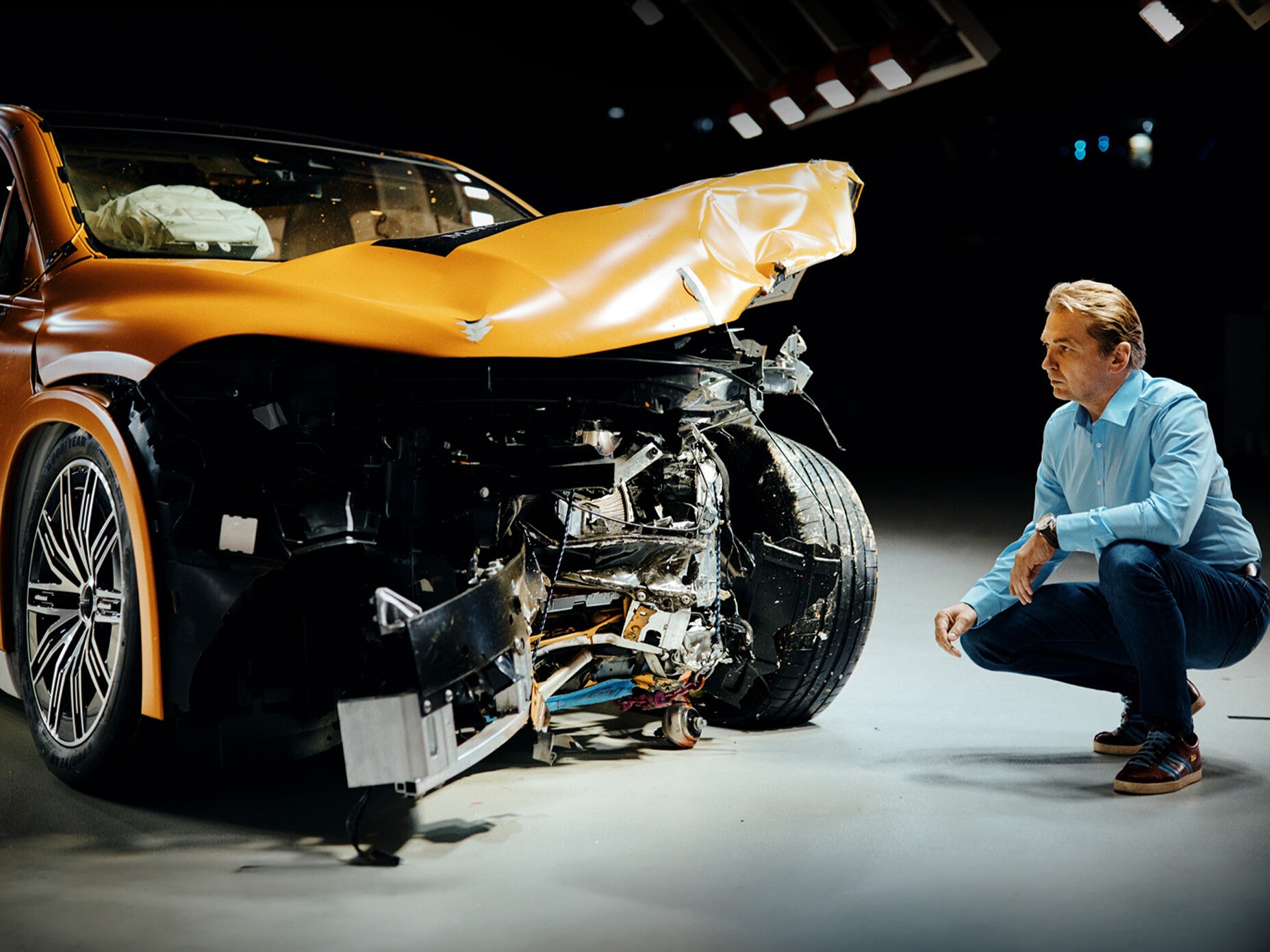 Crashtestexpert inspecteert een frontaal beschadigde Mercedes-Benz terwijl hij ernaast gehurkt zit.