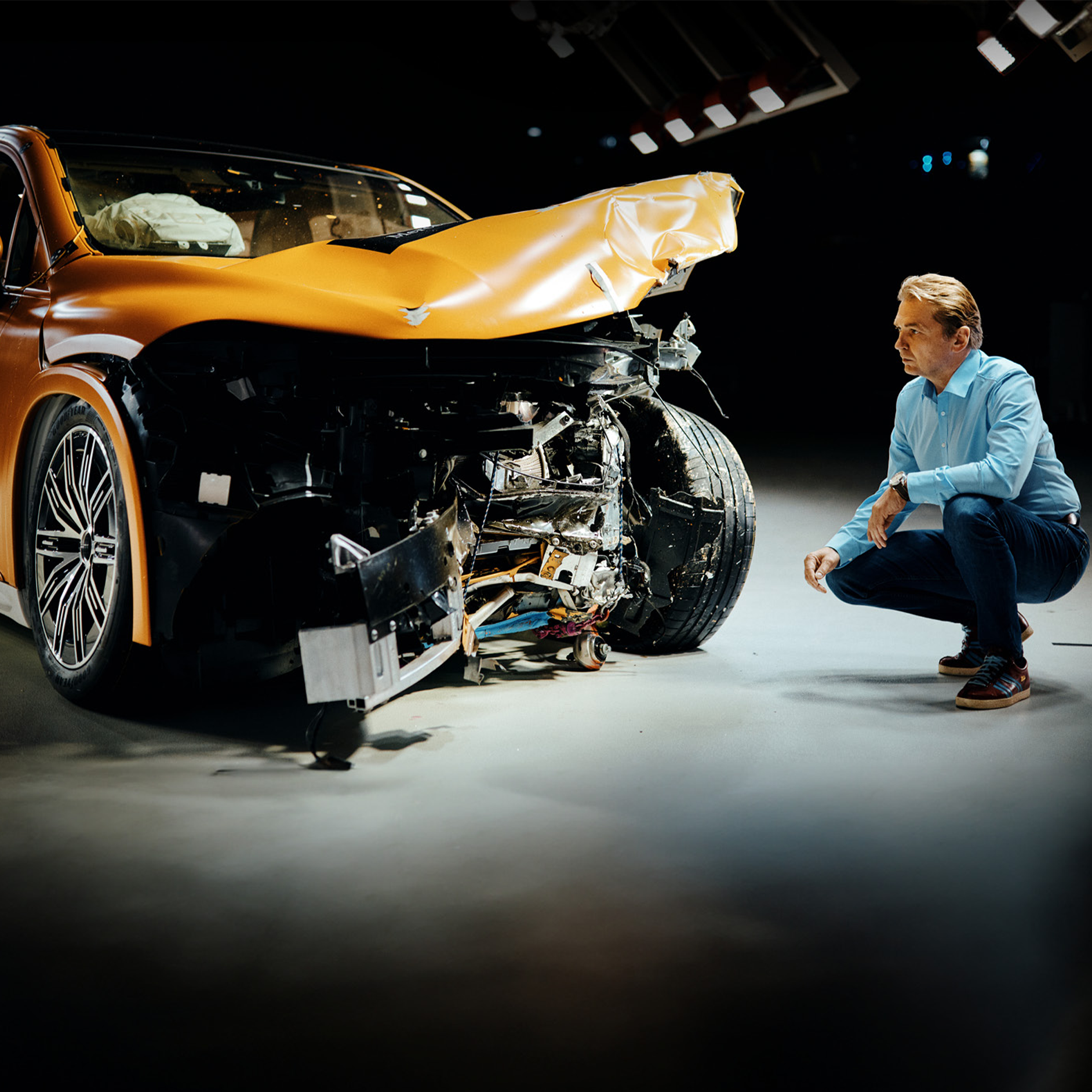 Crashtest experts | Veiligheid | Mercedes-Benz Crashtestexpert inspecteert een frontaal beschadigde Mercedes-Benz terwijl hij ernaast gehurkt zit.