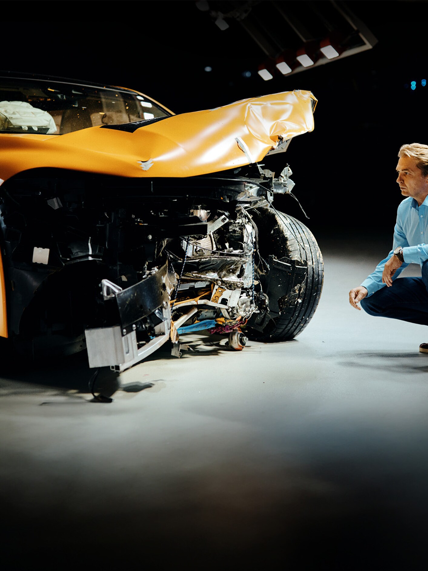 Crashtestexpert inspecteert een frontaal beschadigde Mercedes-Benz terwijl hij ernaast gehurkt zit.