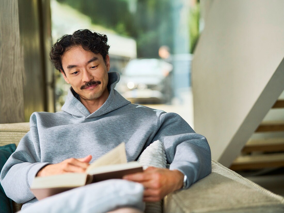 Klant zit binnen een boek te lezen. Door een raam achter hem is te zien dat een specialist een auto onderhoudt.