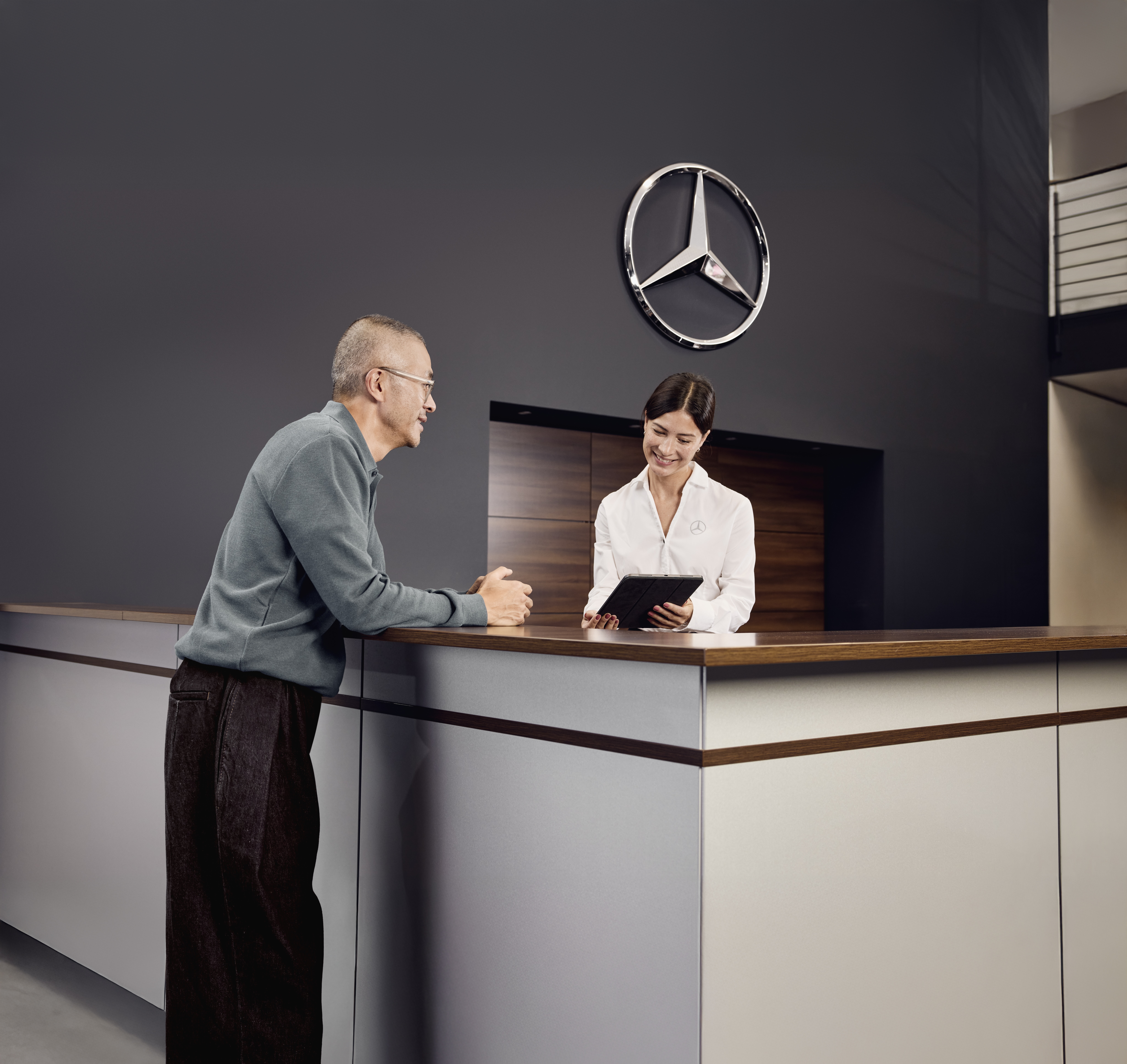 Mercedes-Benz originele onderdelen Servicereceptie bij een Mercedes-Benz dealer waar een klant de onderhoudsdetails van zijn auto bespreekt met een serviceadviseur aan de balie.