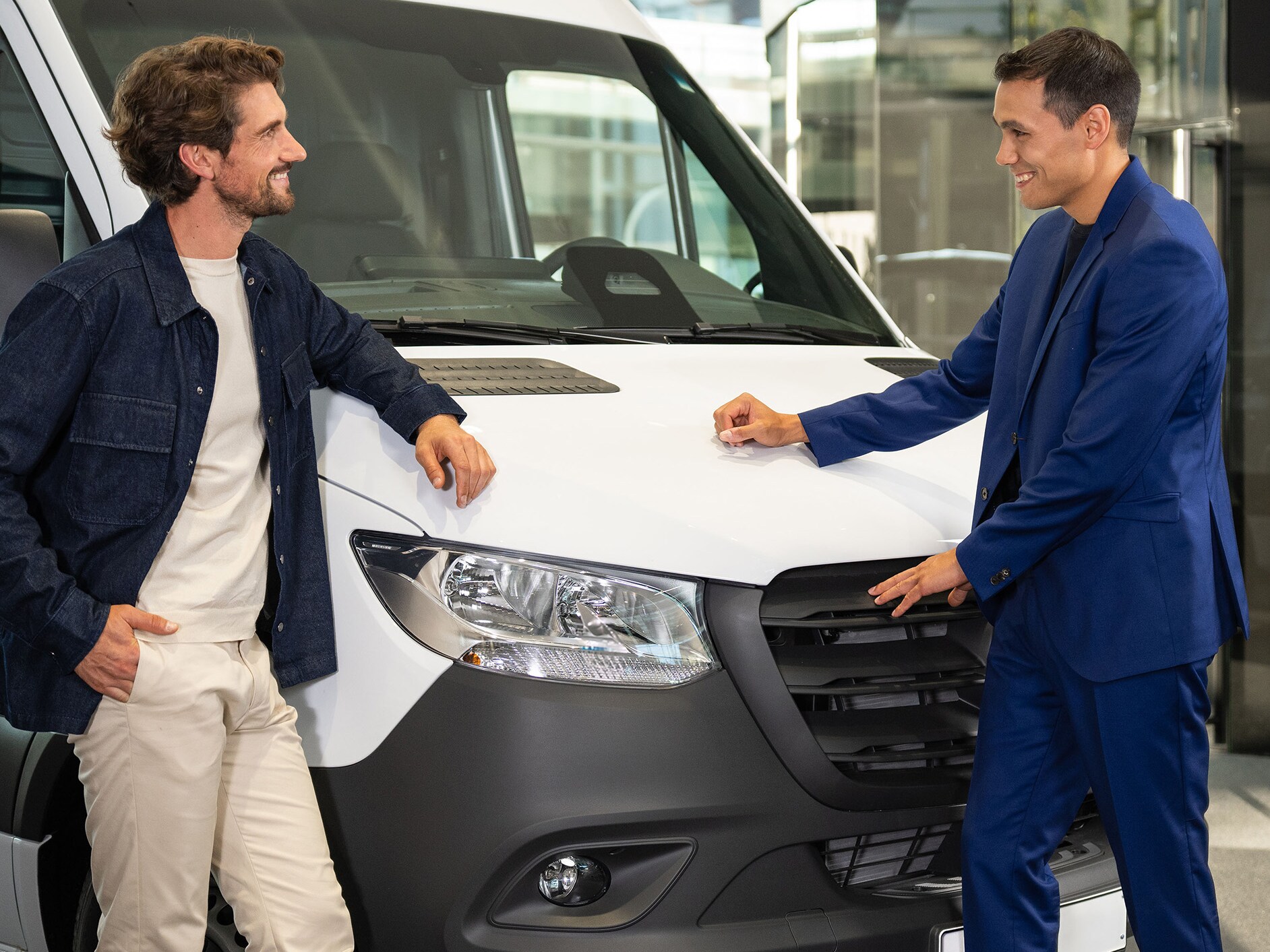 Twee personen leunen tegen een Mercedes-Benz bedrijfswagen en zijn aan het praten.​