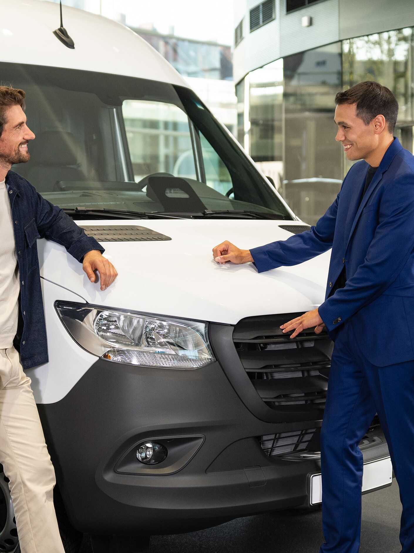 Twee personen leunen tegen een Mercedes-Benz bestelwagen en zijn in gesprek.​