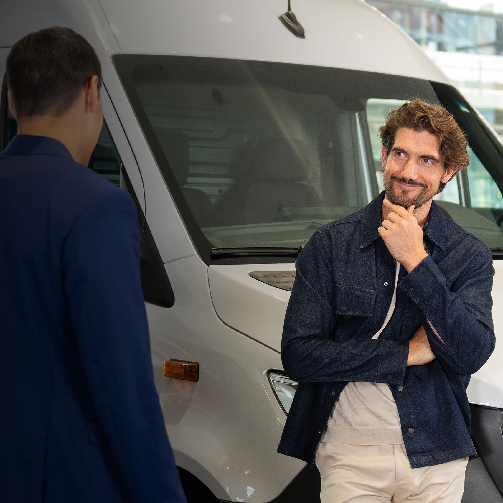 Klant in gesprek met een adviseur naast een witte Mercedes-Benz bedrijfswagen in de showroom.