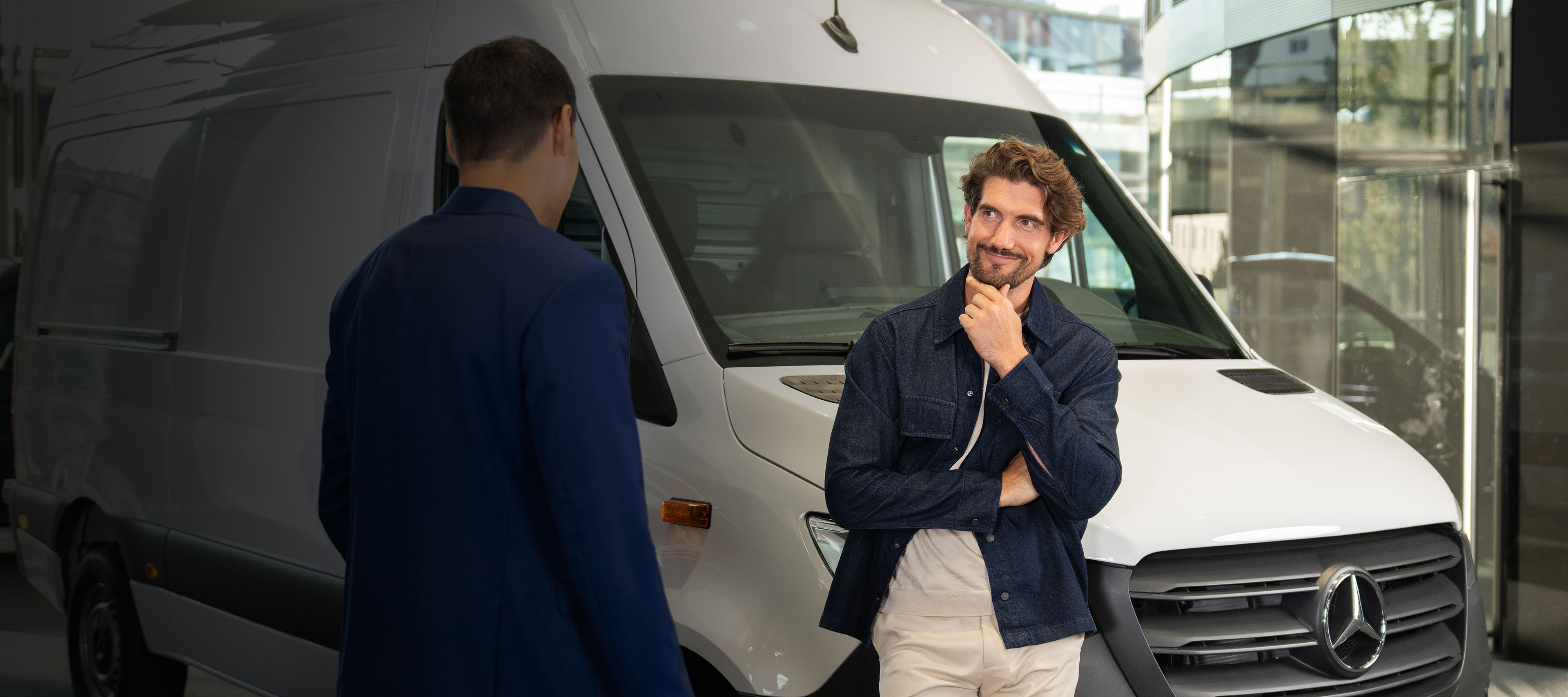 Klant bespreekt bedrijfswagen met adviseur Klant in gesprek met een adviseur naast een witte Mercedes-Benz bedrijfswagen in de showroom.