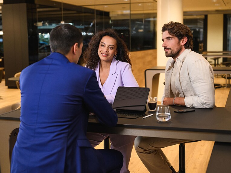 Drie personen zitten aan een tafel en zijn in gesprek.​
