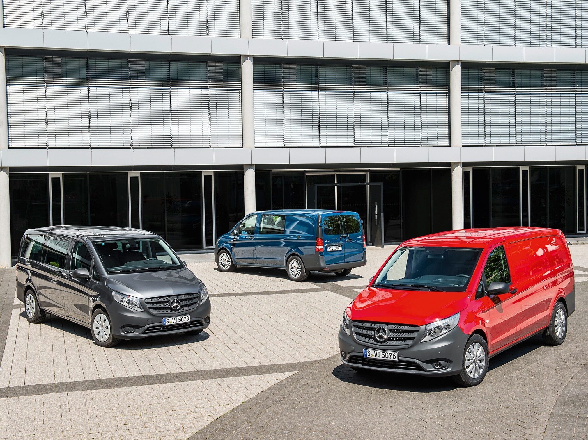 Plusieurs Mercedes-Benz Vito garés devant un immeuble de bureaux moderne