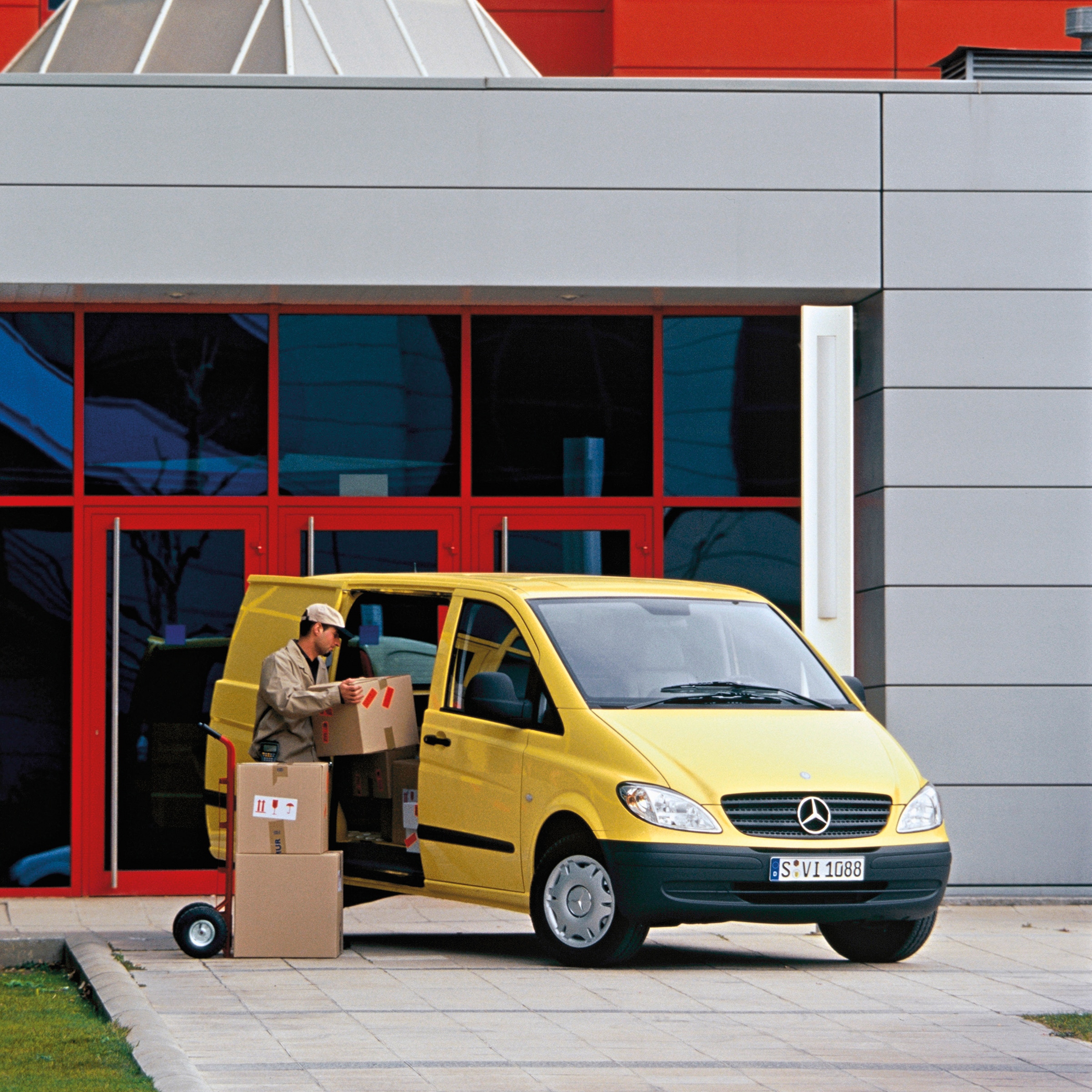 La deuxième génération de Mercedes-Benz Vito | Histoire des véhicules industriels | Mercedes-Benz Un Mercedes-Benz Vito jaune garé devant un immeuble, avec un employé en train de décharger des colis