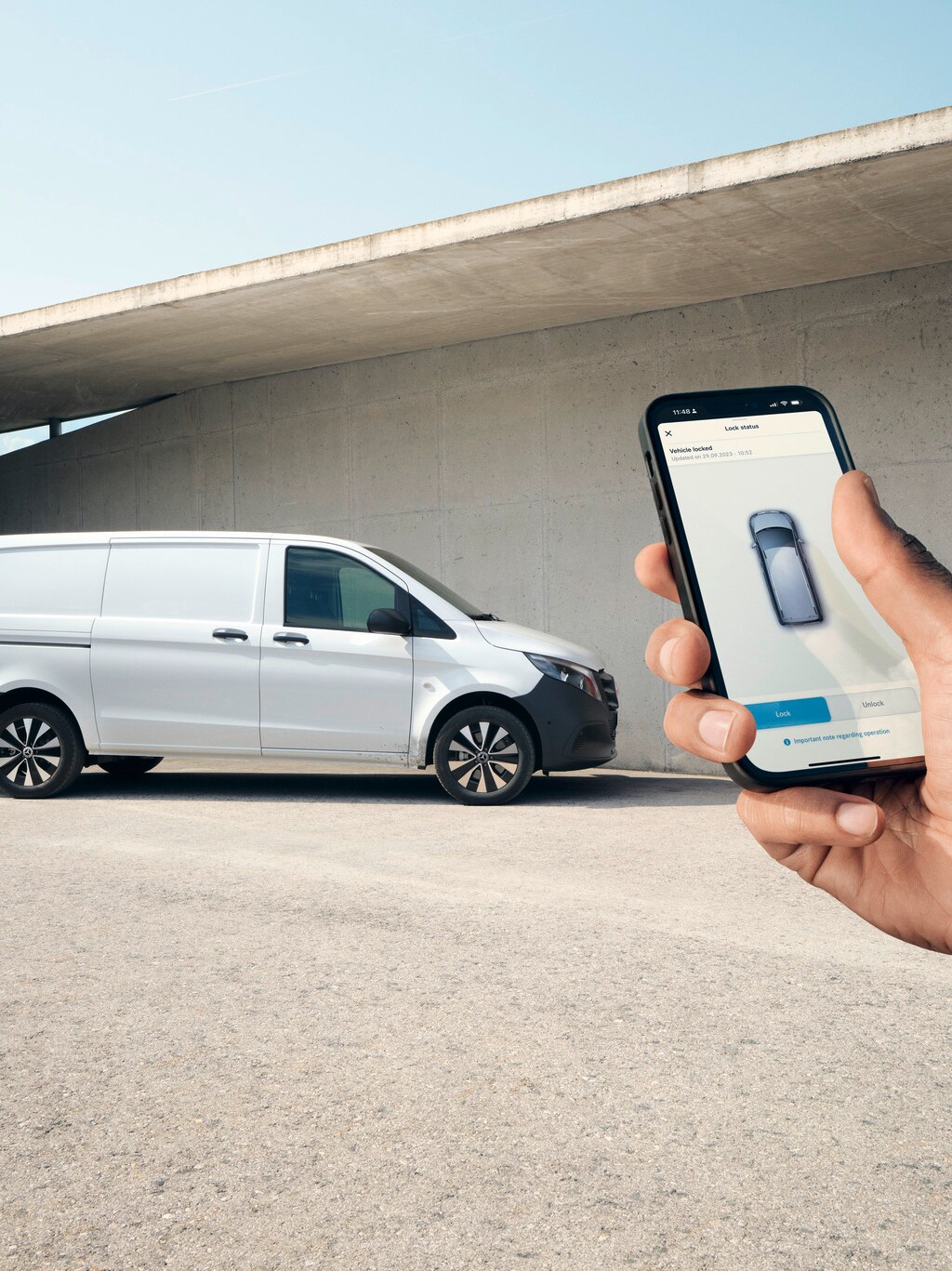 Hand met een smartphone die de Mercedes me App toont. Vito Gesloten Bestelwagen op de achtergrond.