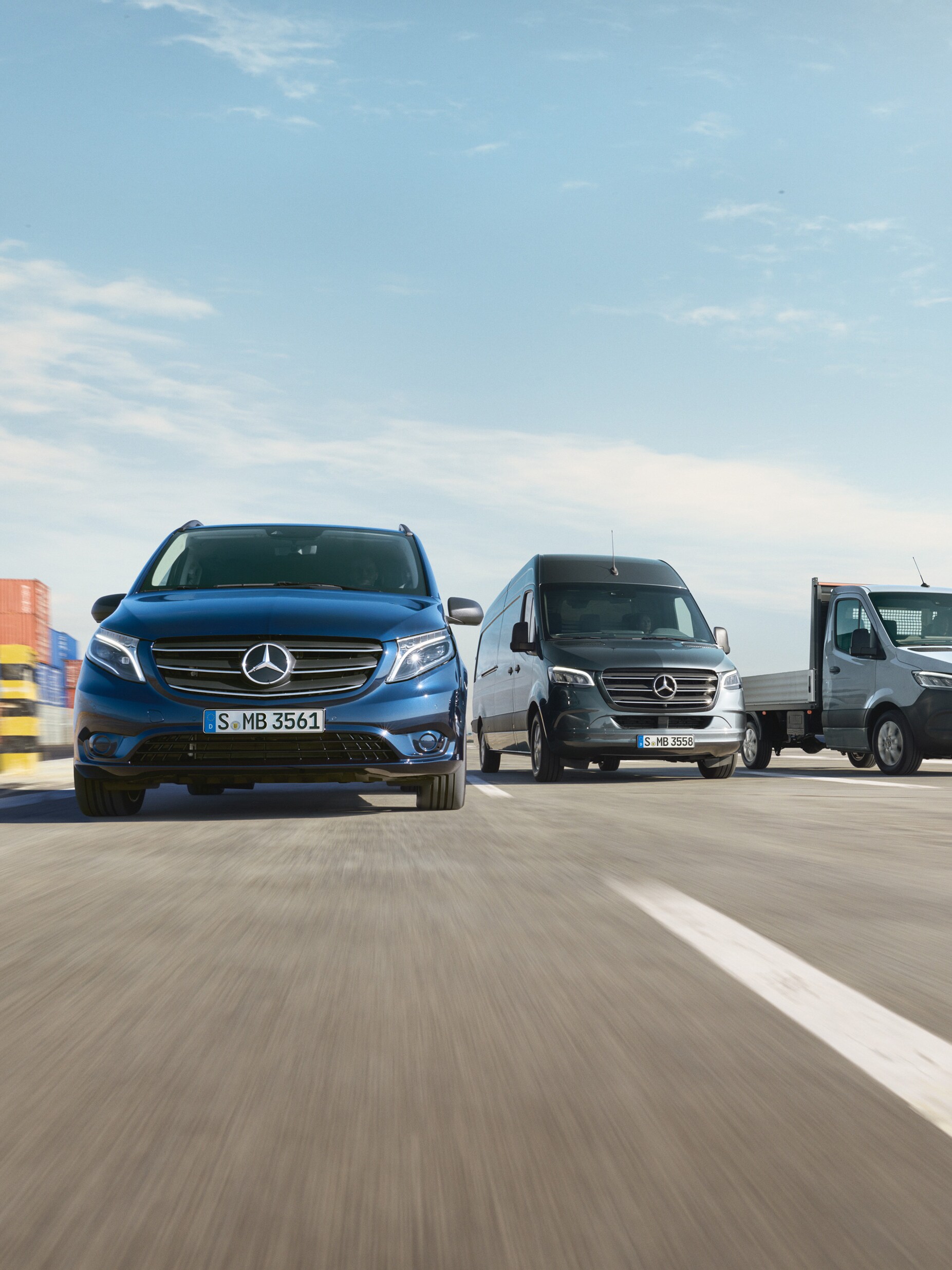 Une série d’utilitaires légers Mercedes-Benz garés côte à côte sur une route à côté d'un quai d'expédition.