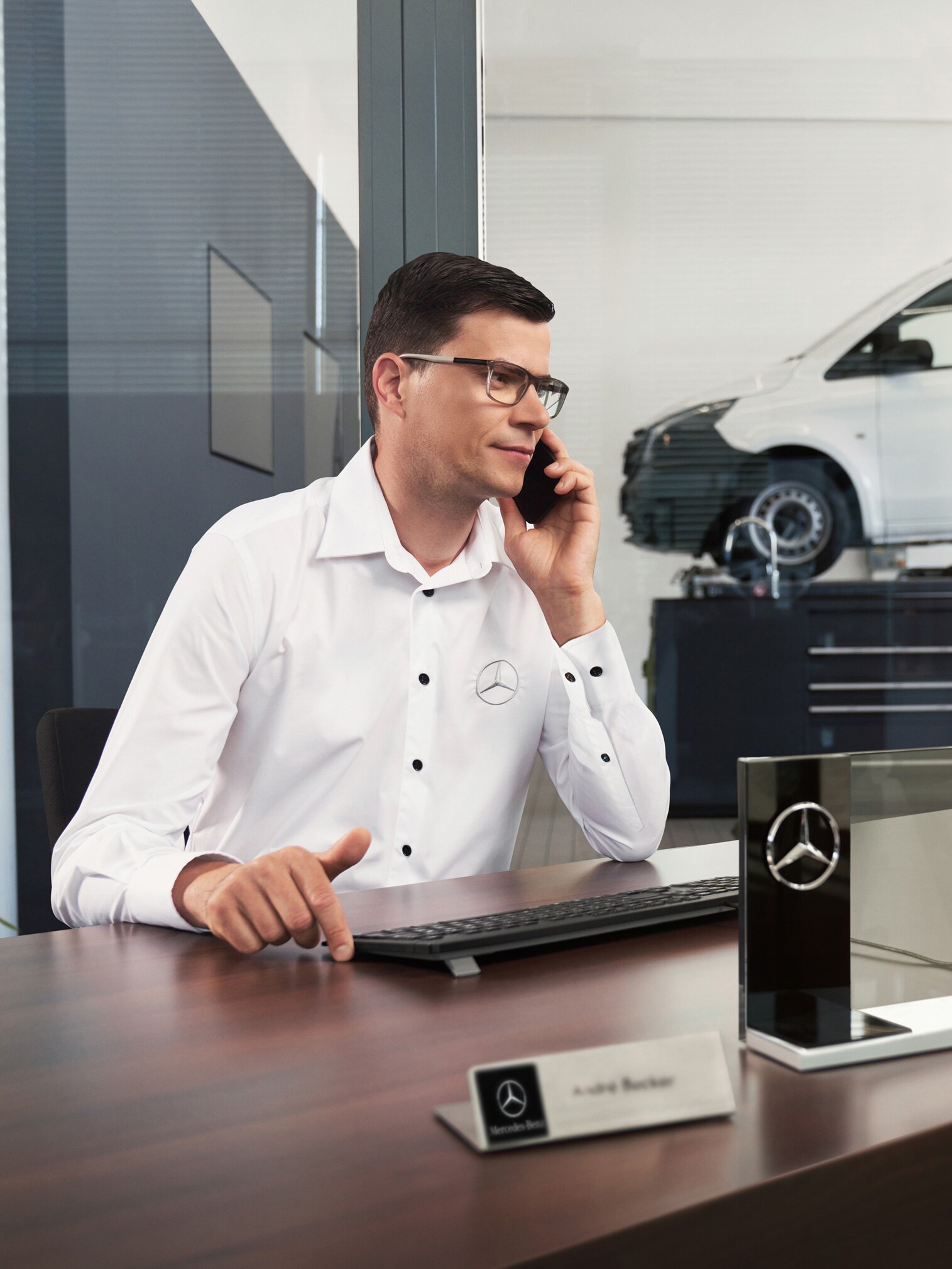 Mercedes-Benz medewerker telefoneert aan een bureau met een Mercedes-Benz Vito bestelwagen in de werkplaats.