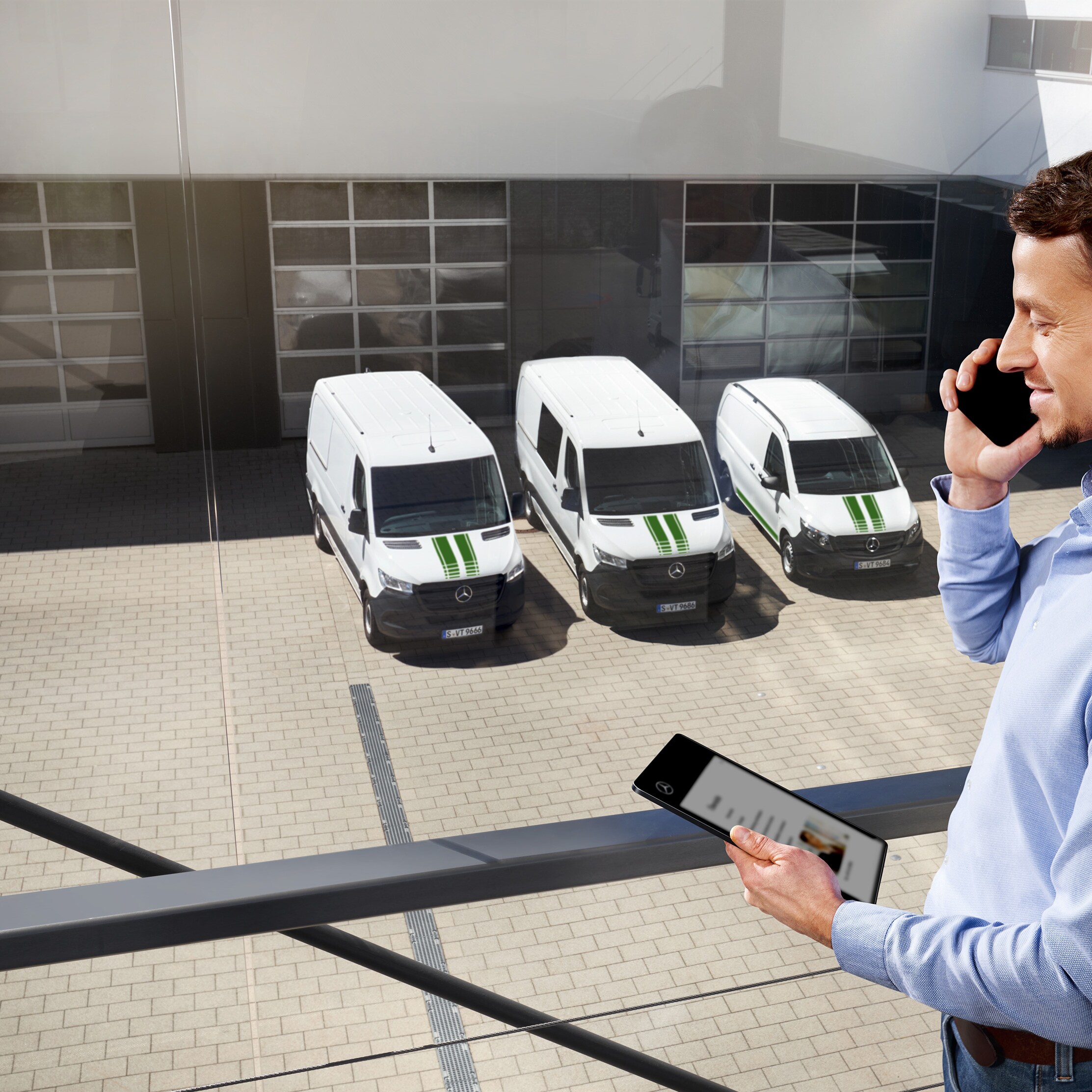 Client au téléphone devant une flotte d'utilitaires légers Mercedes-Benz blancs.