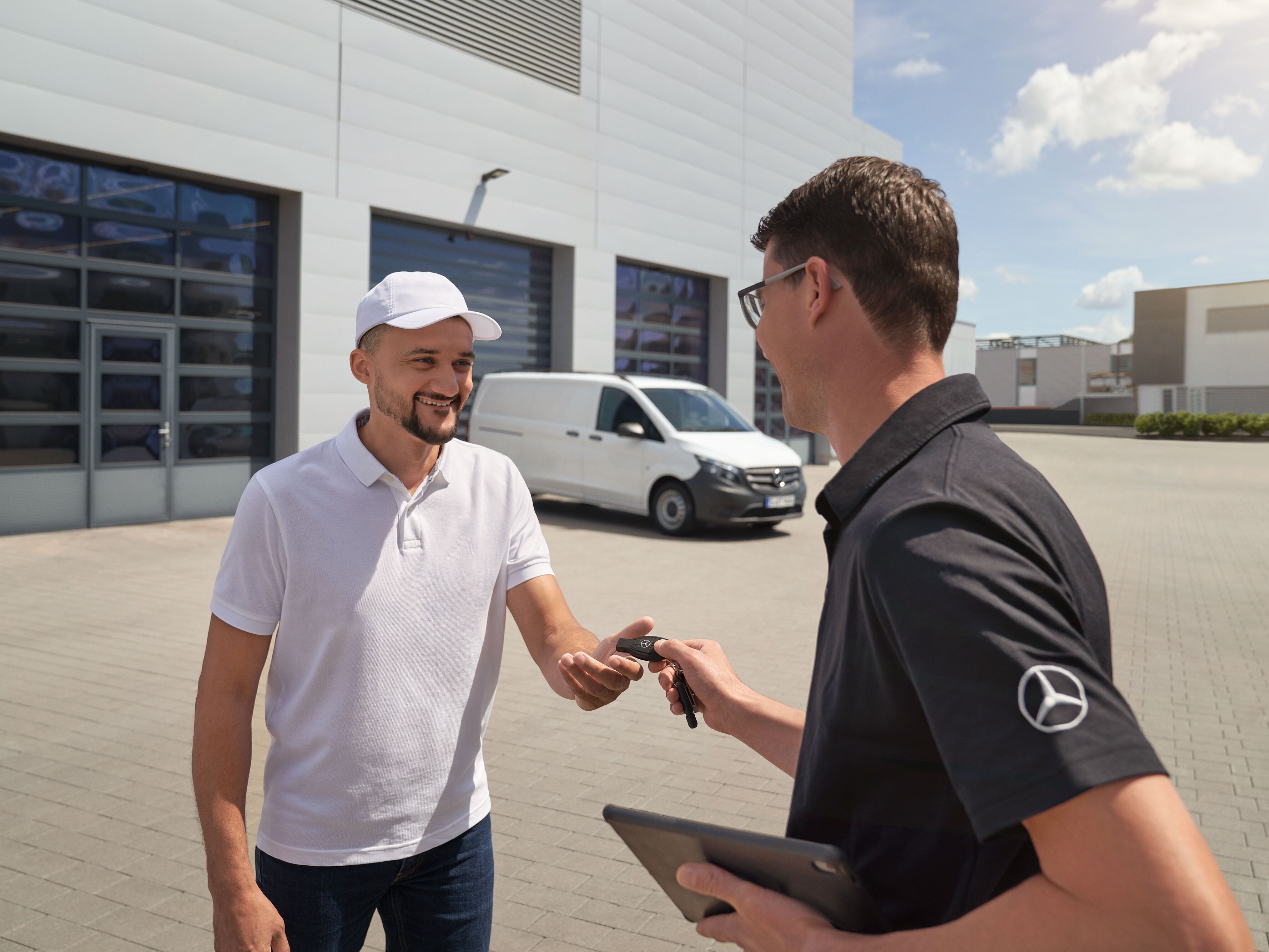 Mercedes-Benz technicus overhandigt sleutels aan een klant met een witte Mercedes-Benz Vito bedrijfswagen op de achtergrond.