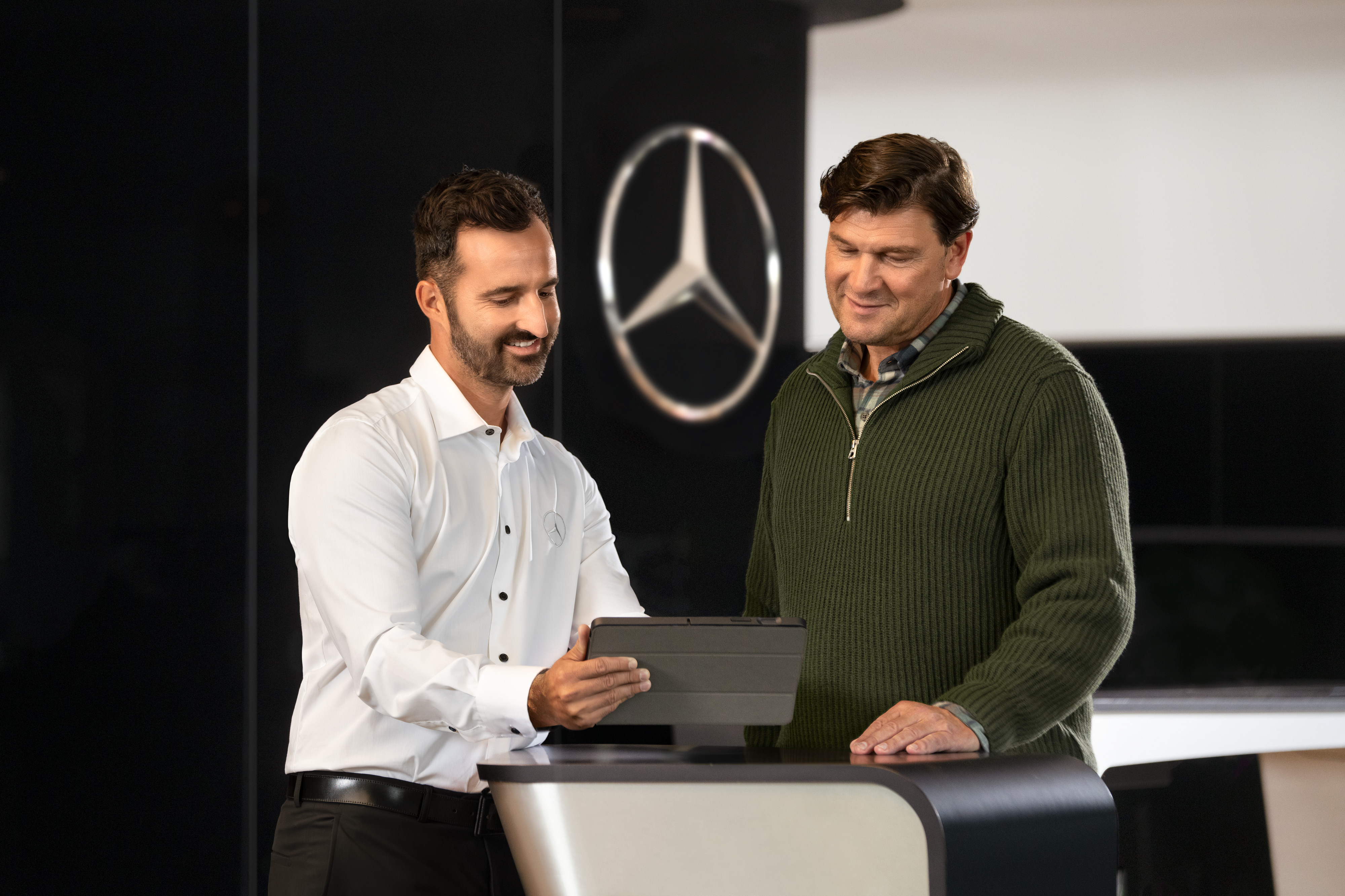 Mercedes-Benz | Confort | Partenaire de service Un employé Mercedes-Benz discute avec un client tout en regardant un appareil posé sur une table.