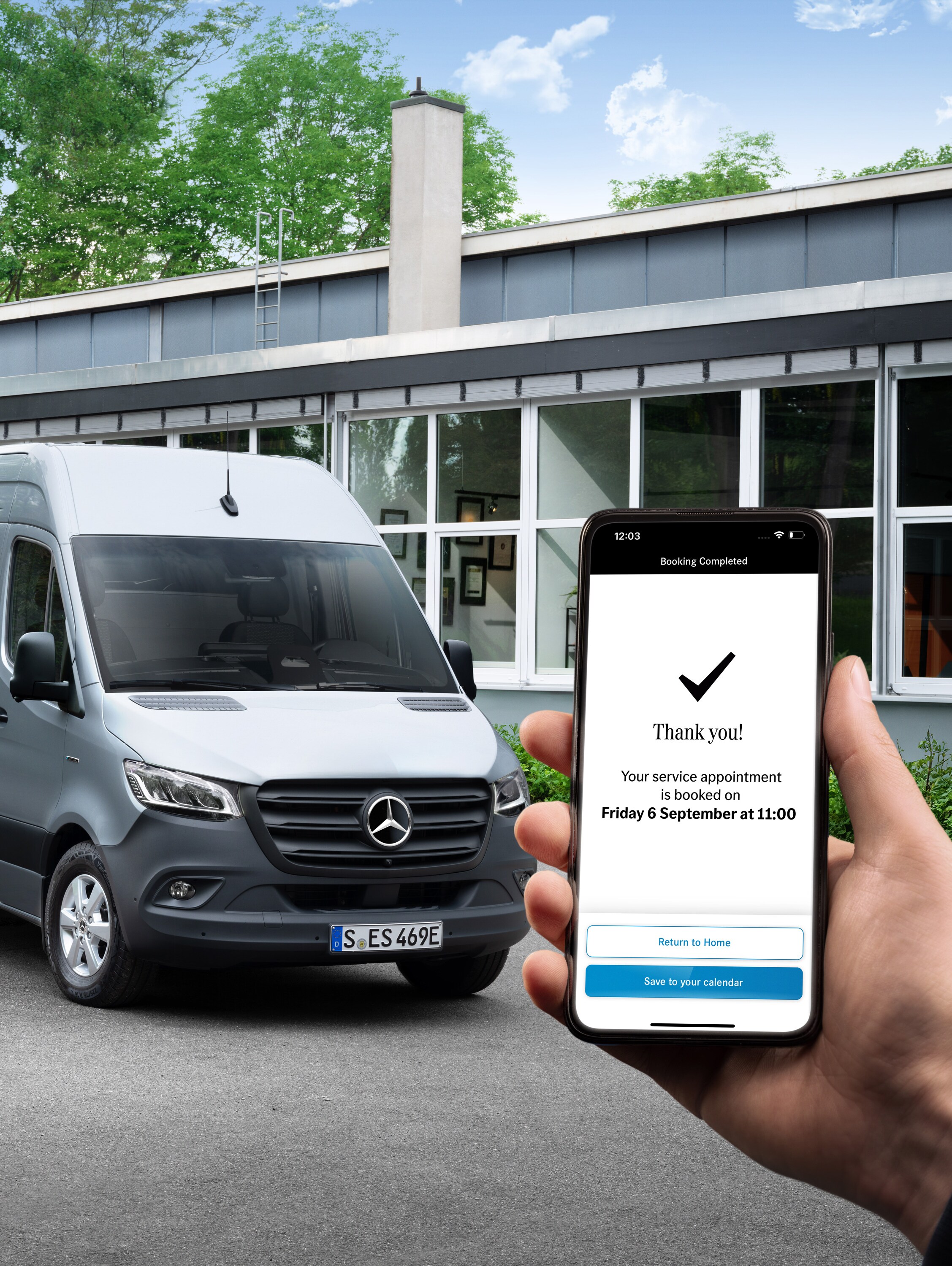 Un utilitaire léger Mercedes-Benz Sprinter gris devant un bureau avec, au premier plan, une personne tenant un smartphone.