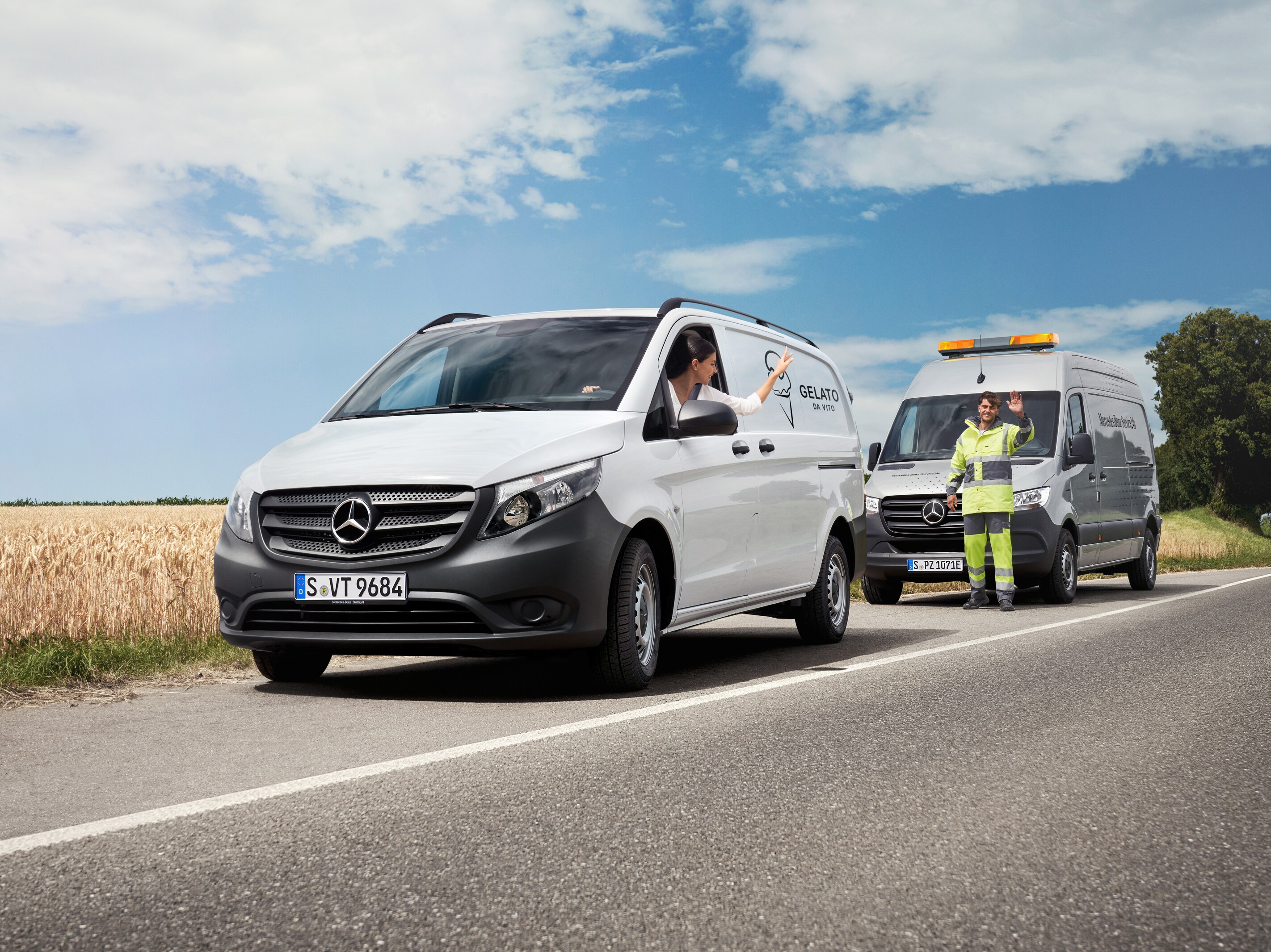 Een vrouw in een witte Mercedes-Benz Vito zwaait naar een Mercedes-Benz servicemonteur langs de kant van de weg.