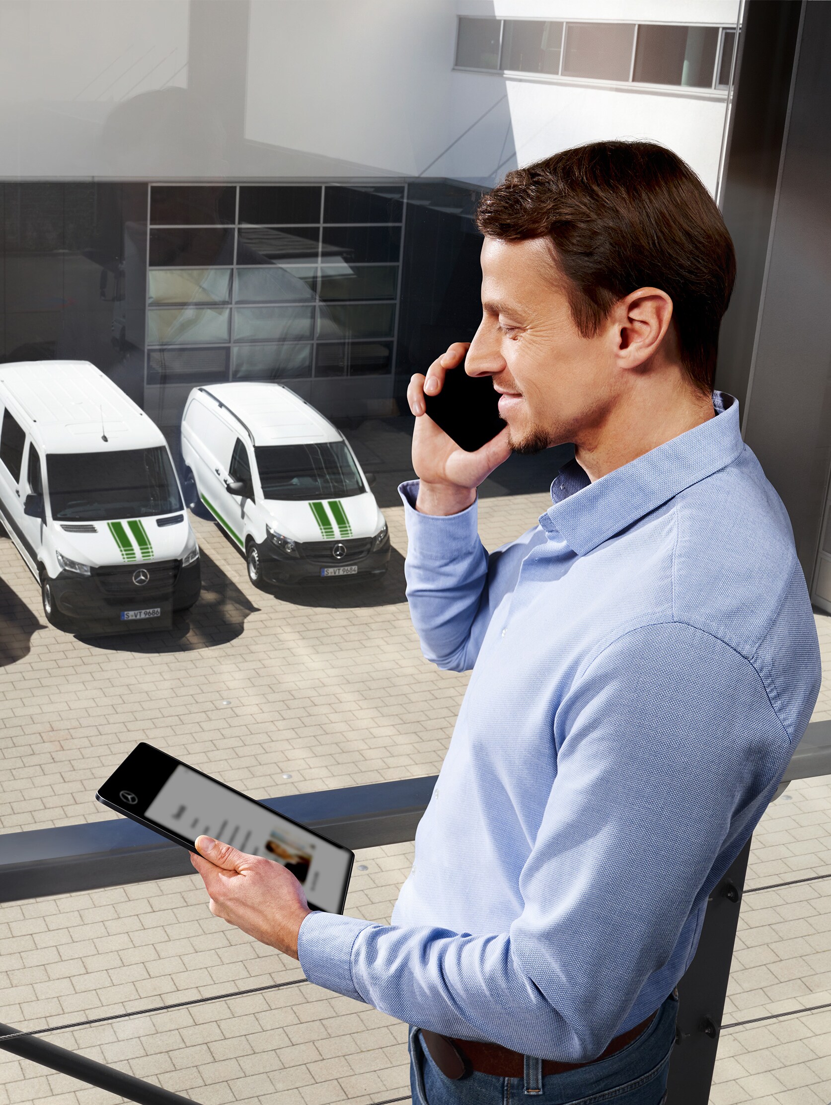 Homme au téléphone avec une tablette devant trois utilitaires légers Mercedes-Benz. Sujet&nbsp;: quelle est la durée de la garantie constructeur chez Mercedes-Benz&nbsp;?