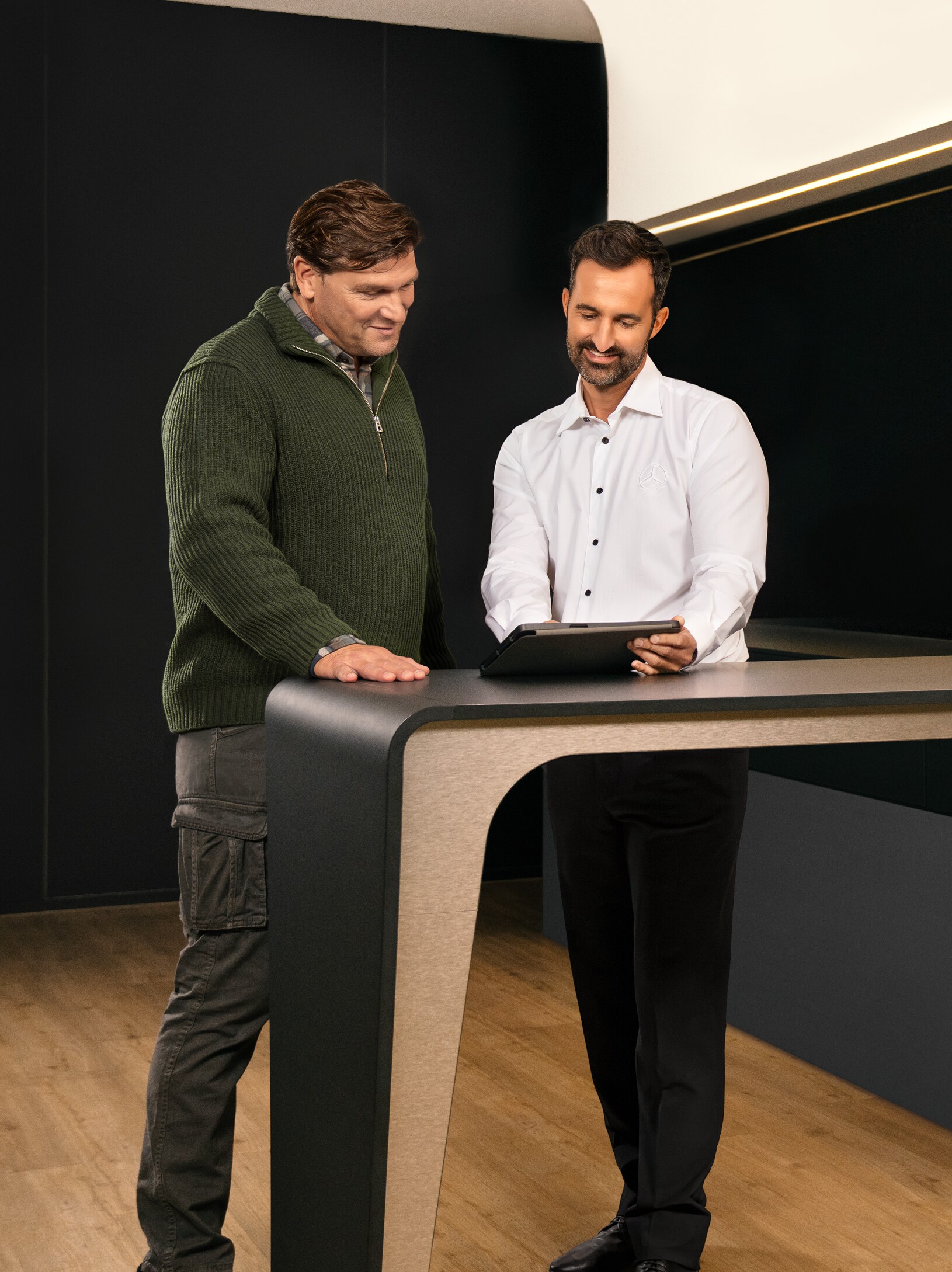 Twee mannen in overleg rond een tafel terwijl ze naar een iPad kijken.