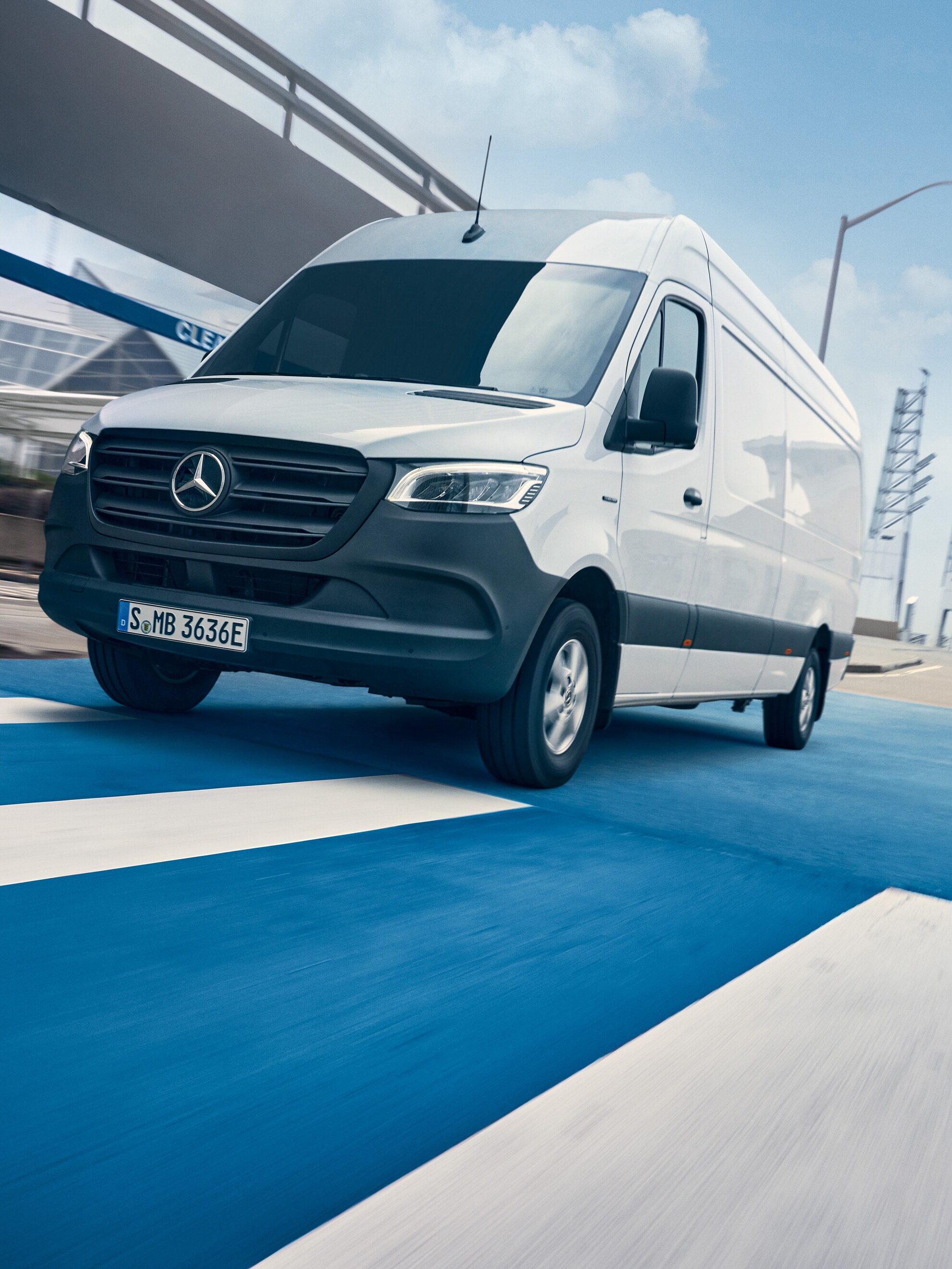 Une Mercedes-Benz Sprinter blanche roule sur une route dans une ville.