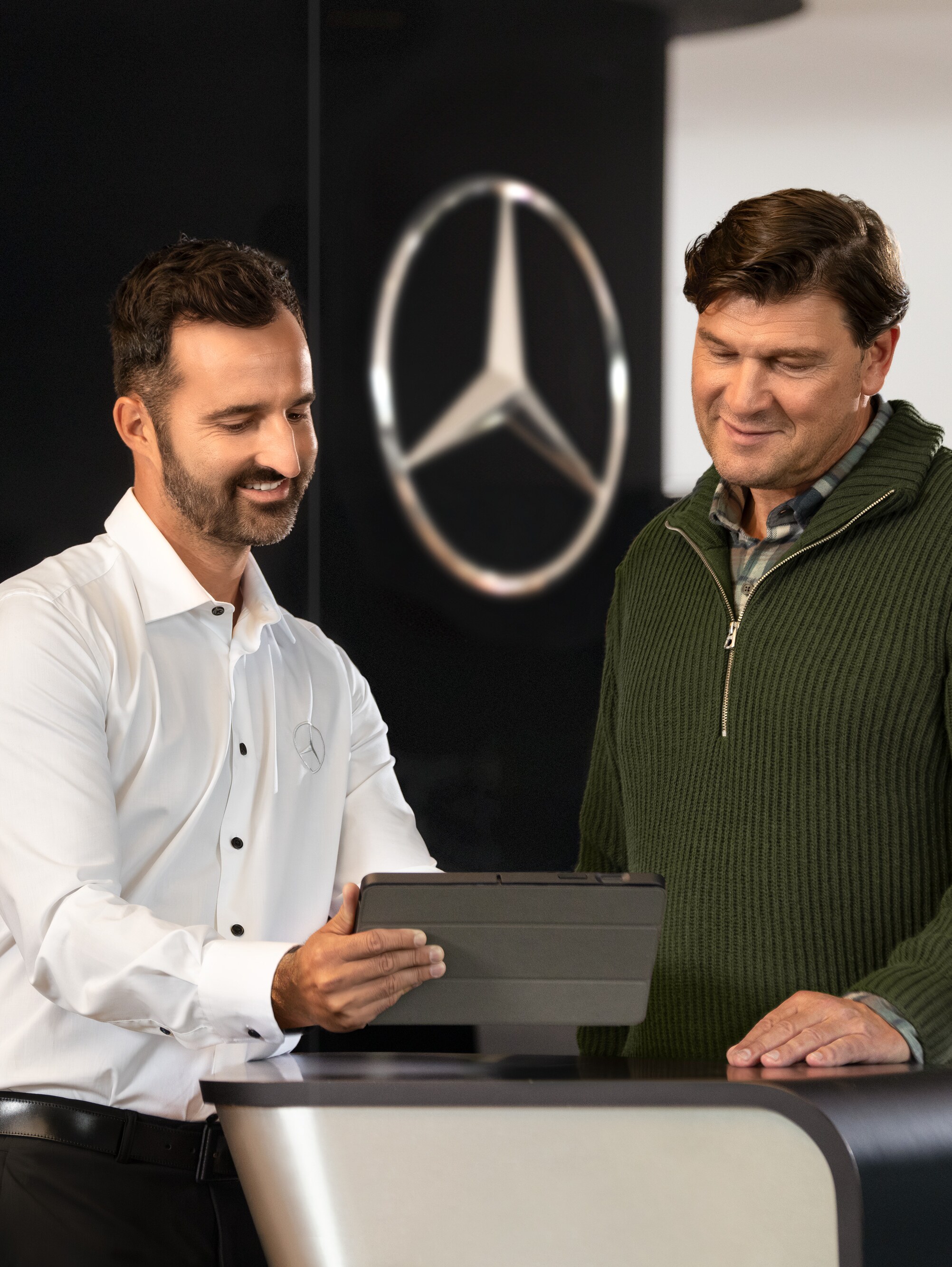 Twee mannen praten aan een balie terwijl ze op een tablet kijken, voor de ster van Mercedes-Benz.