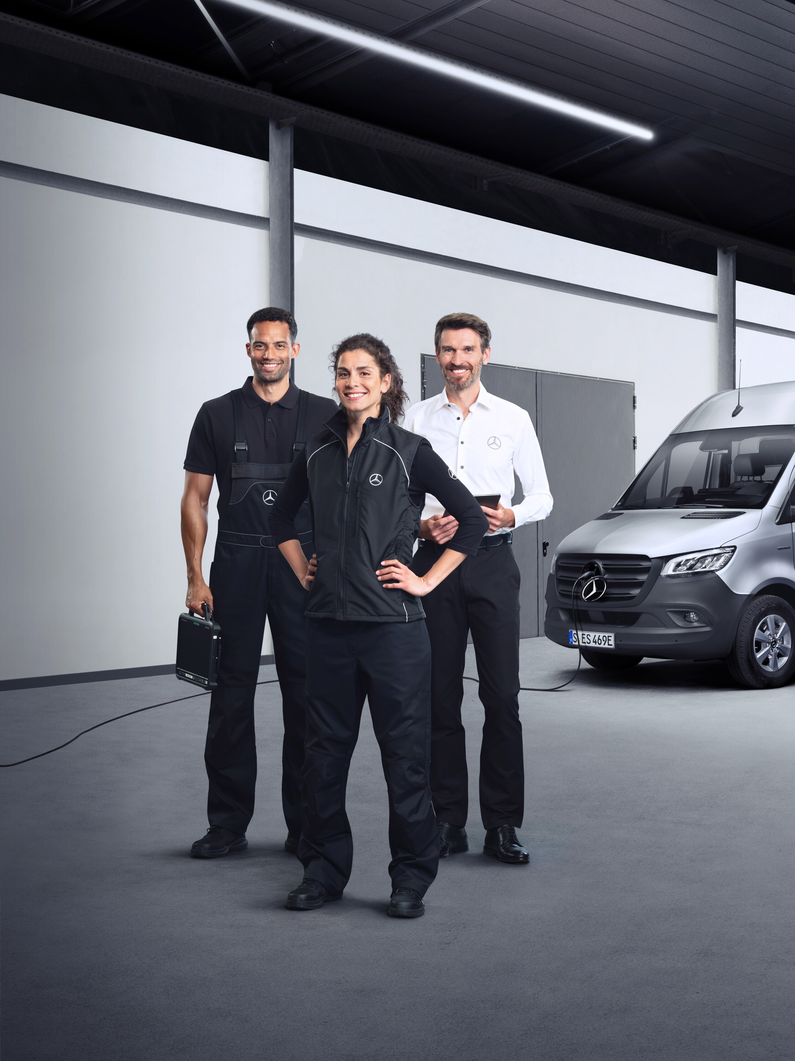 Drie medewerkers die voor een zilveren Mercedes-Benz eSprinter staan met aangesloten laadkabel.