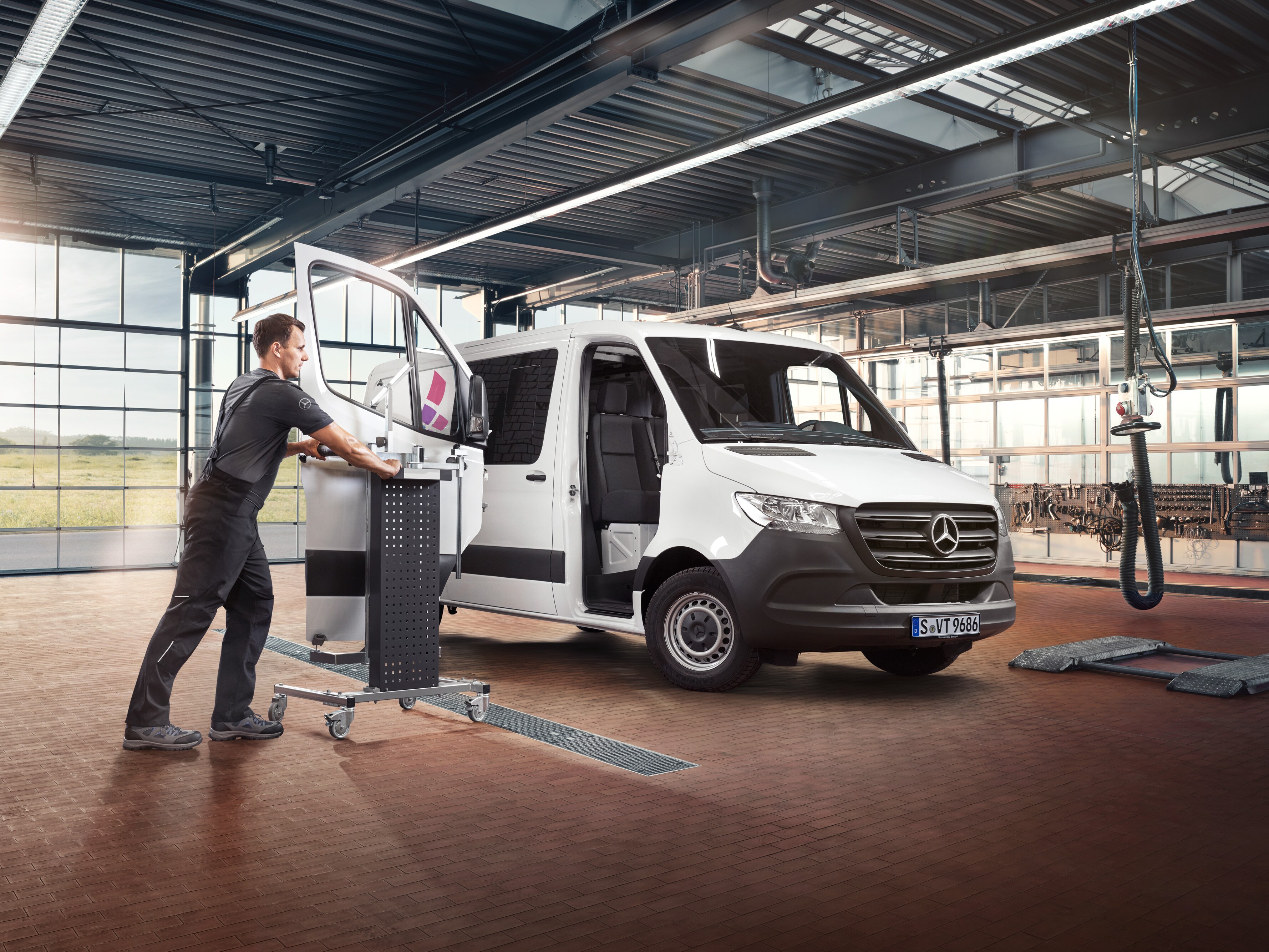 Monteur repareert de passagiersdeur van een witte Mercedes-Benz Sprinter Gesloten Bestelwagen in de werkplaats.