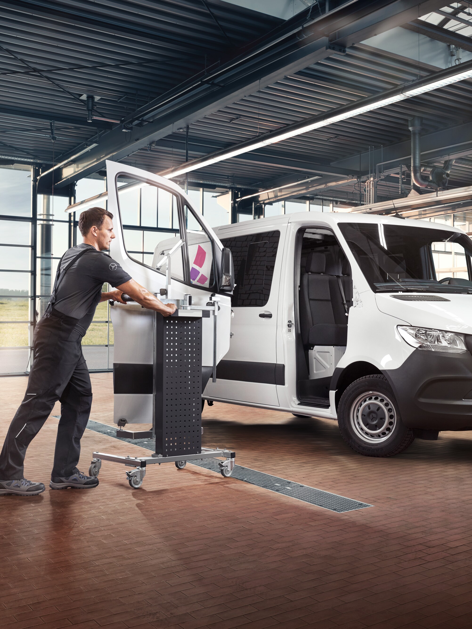 Een monteur onderhoudt de bijrijdersdeur van een witte Mercedes-Benz Sprinter.