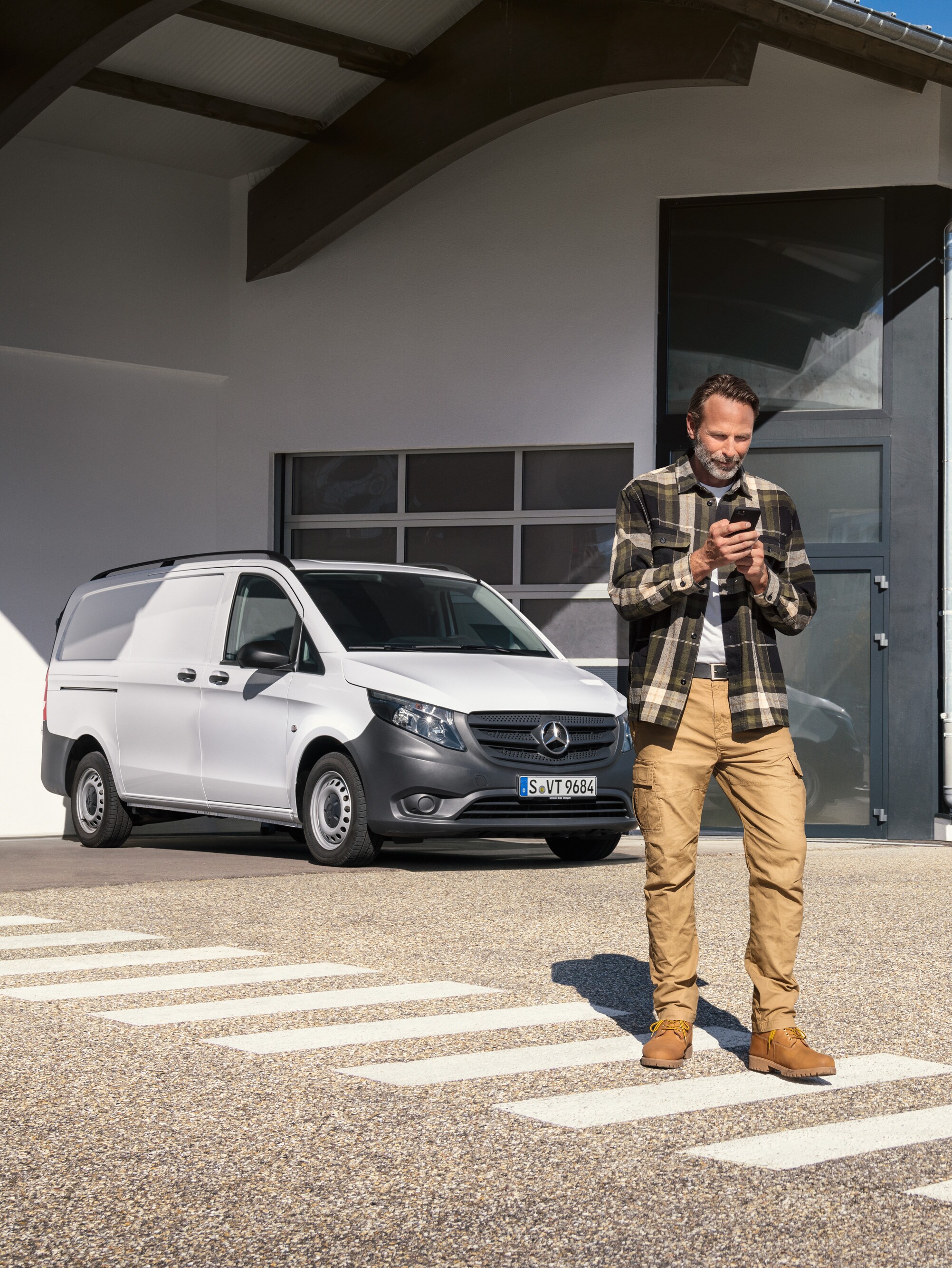 Een man die voor een witte Mercedes-Benz Vito bedrijfswagen staat en zijn smartphone gebruikt.