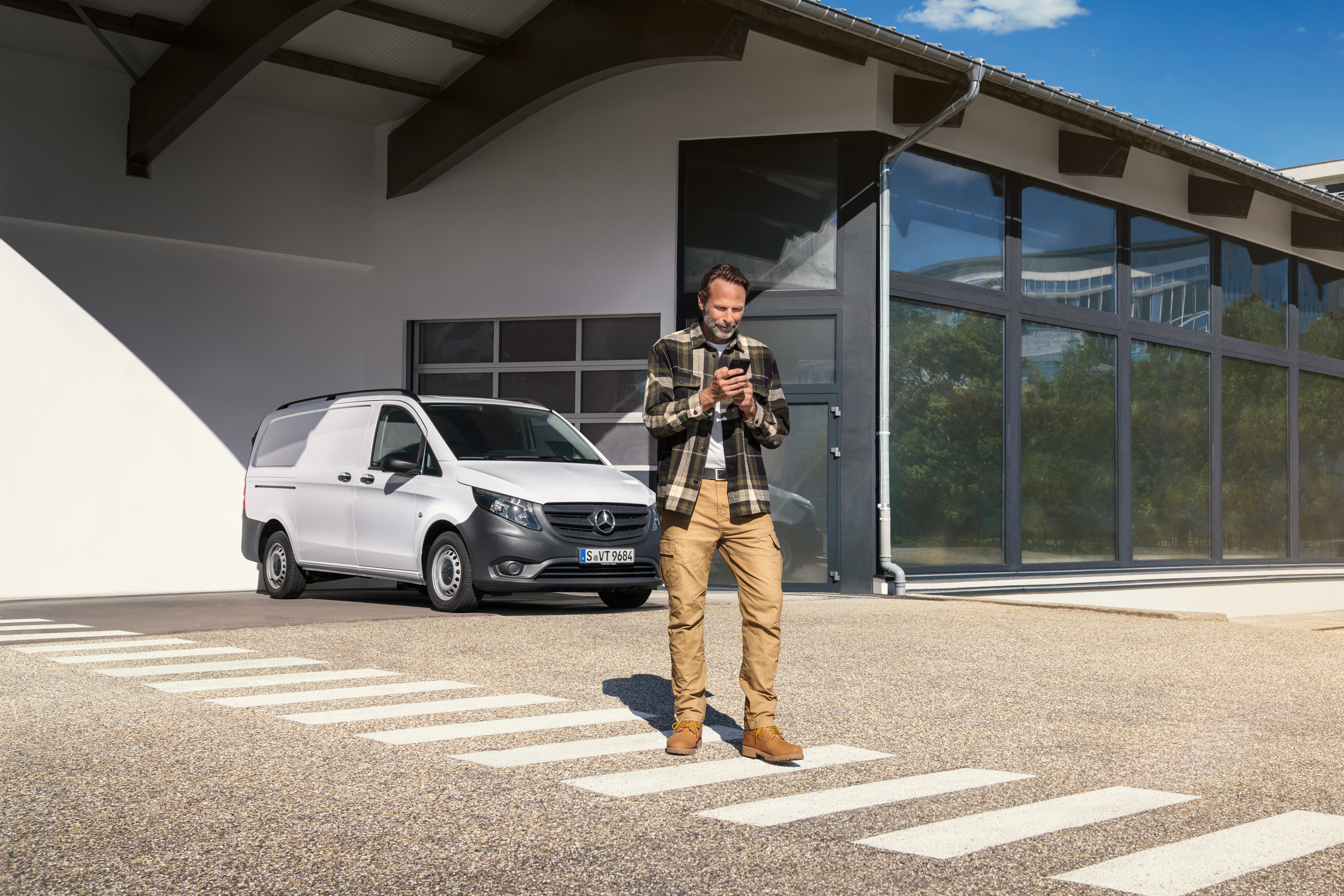 Mercedes-Benz | Service voor elektrische voertuigen | Digitale ondersteuning Een man die voor een witte Mercedes-Benz Vito bedrijfswagen staat en zijn smartphone gebruikt.