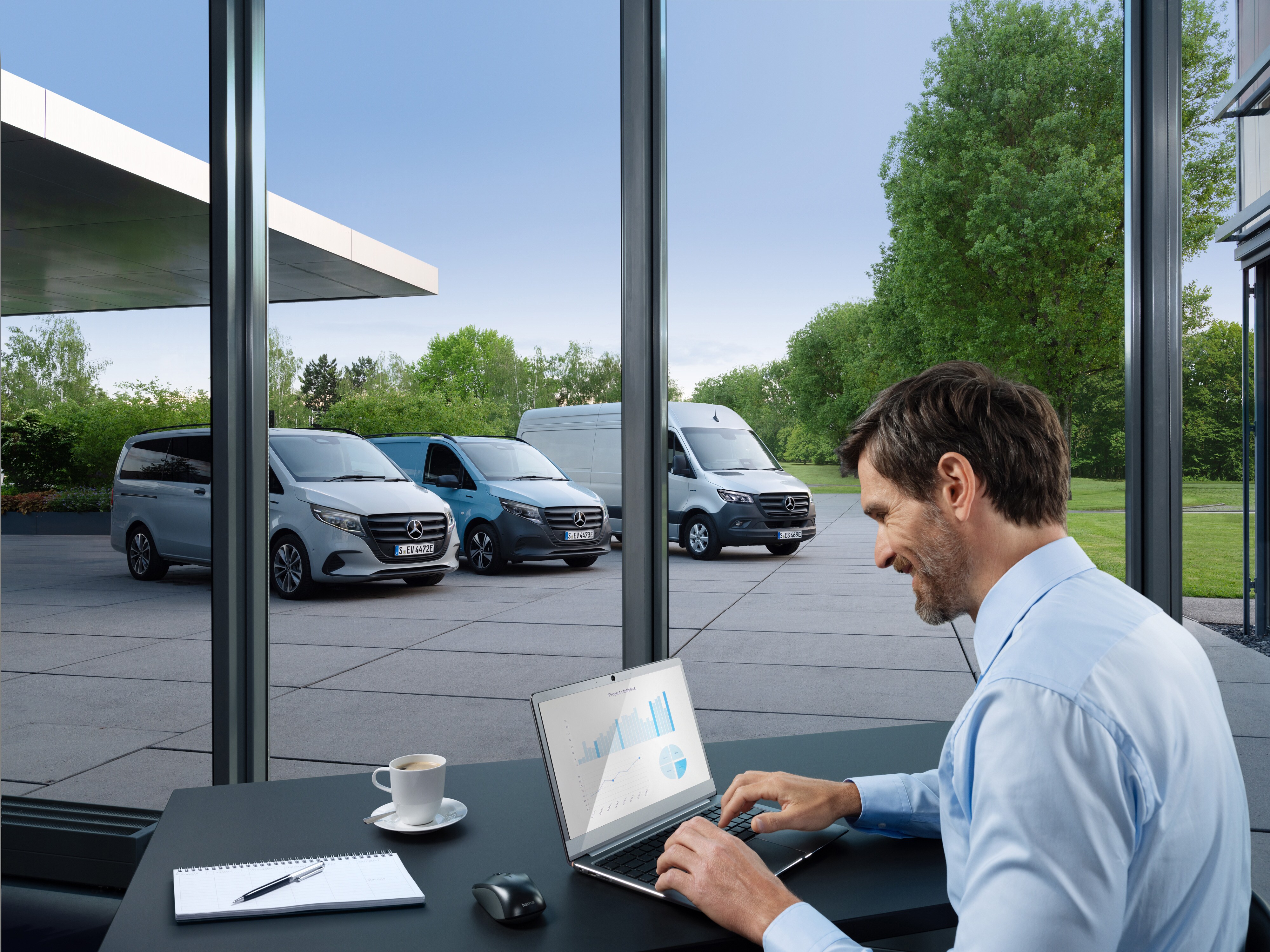 Een man die op een laptop werkt, buiten staat een reeks Mercedes-Benz Bedrijfswagens.