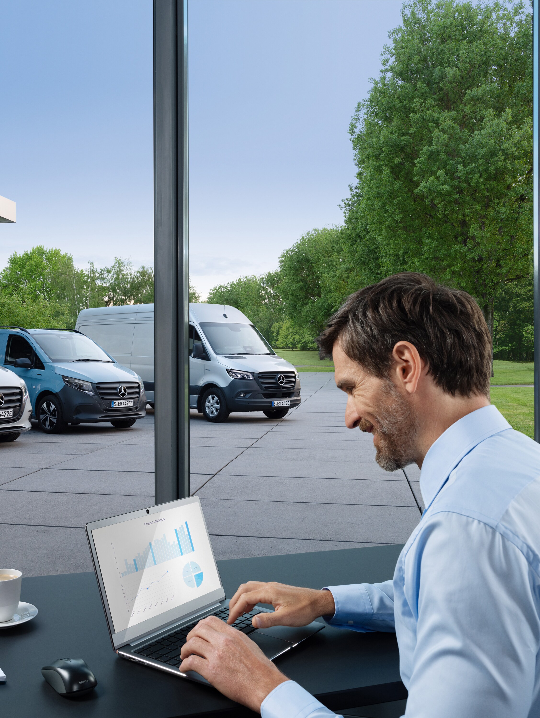 Een man die op een laptop werkt, buiten staat een reeks Mercedes-Benz bedrijfswagens.