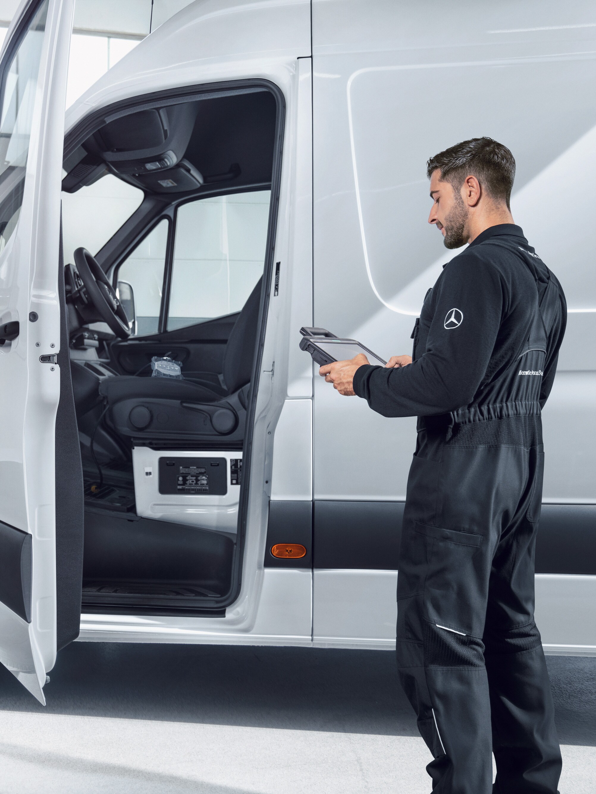 Un technicien contrôle l'état d'un utilitaire léger Mercedes-Benz Sprinter blanc à l'aide d'une tablette.